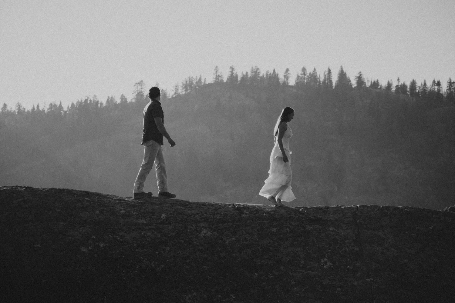Two silhouetted figures walk along a misty hilltop ridge against a moody gray sky.