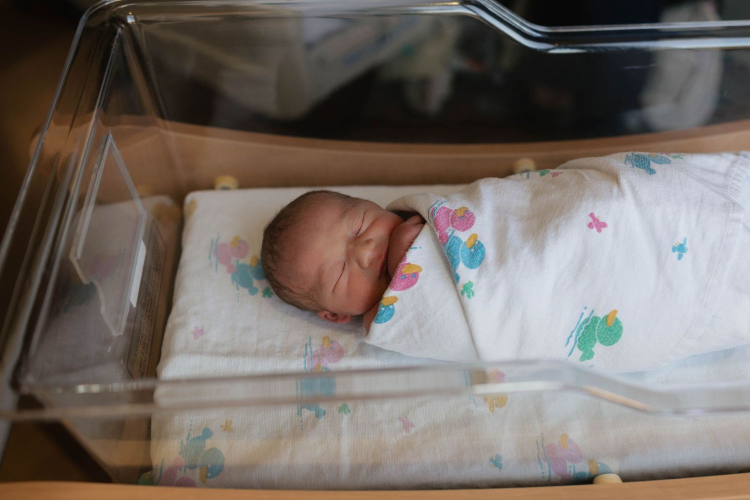 Newborn baby sleeping peacefully in a hospital bassinet with patterned blanket.