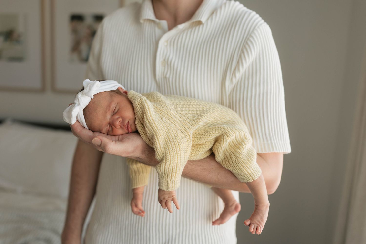 A parent in a white sweater holds a sleeping newborn baby wearing a soft yellow outfit.