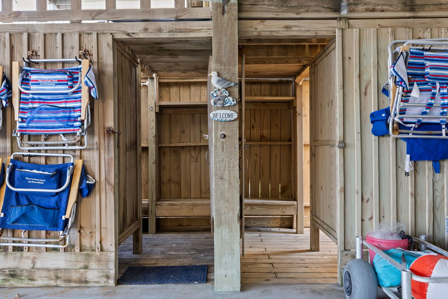 Rustic wooden beach house exterior with open doors, blue folding chairs, and coastal storage area.