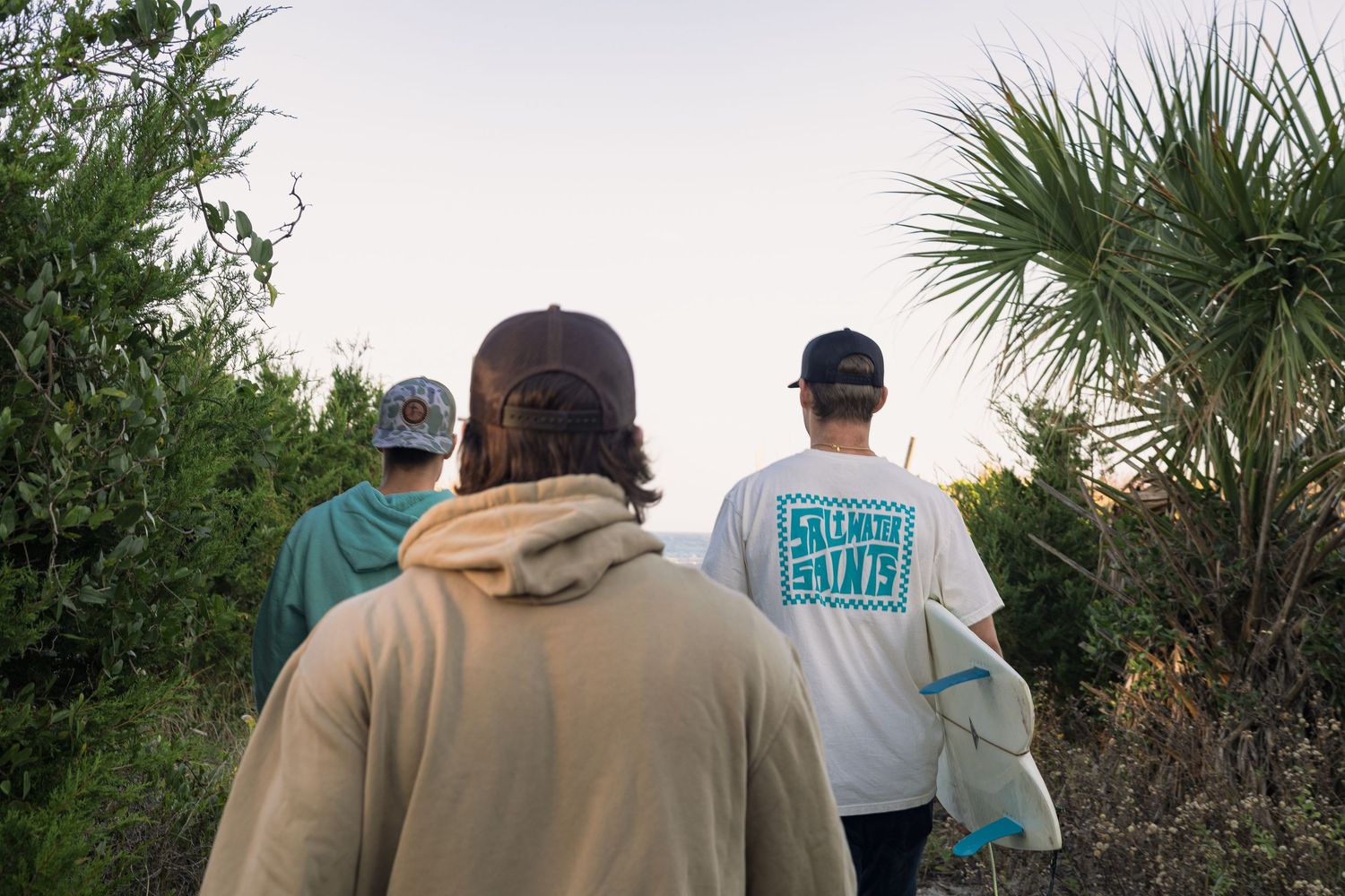 Group of people walking along a palm-lined trail at sunset.