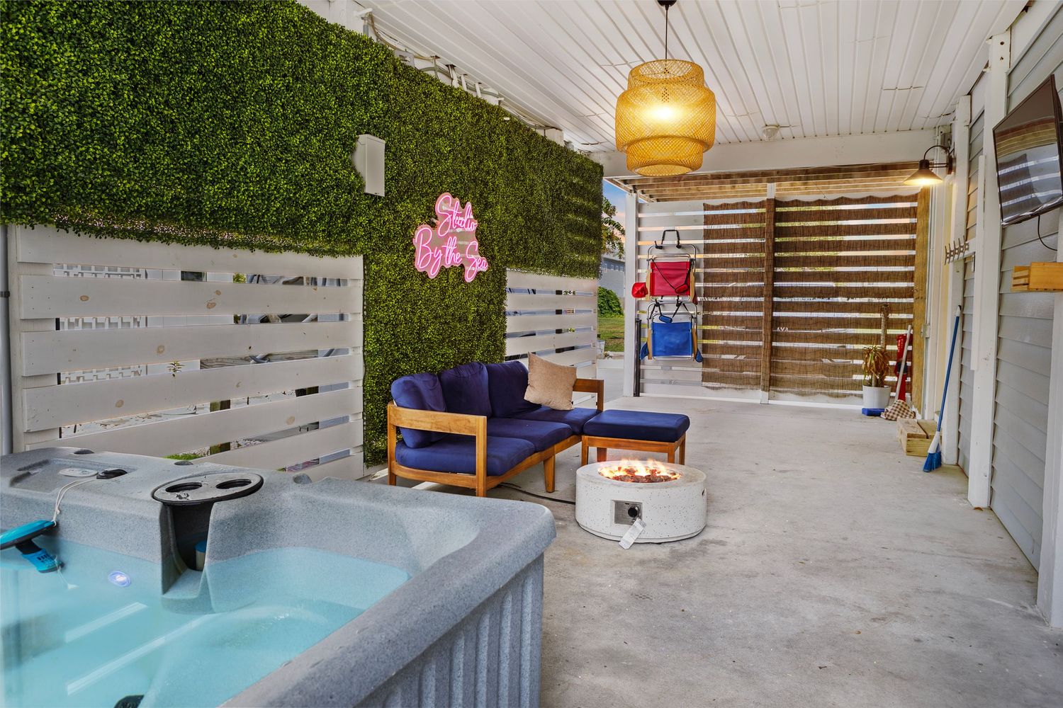Outdoor patio with hot tub, cozy seating, fire pit, green hedge wall, and decorative pendant light.