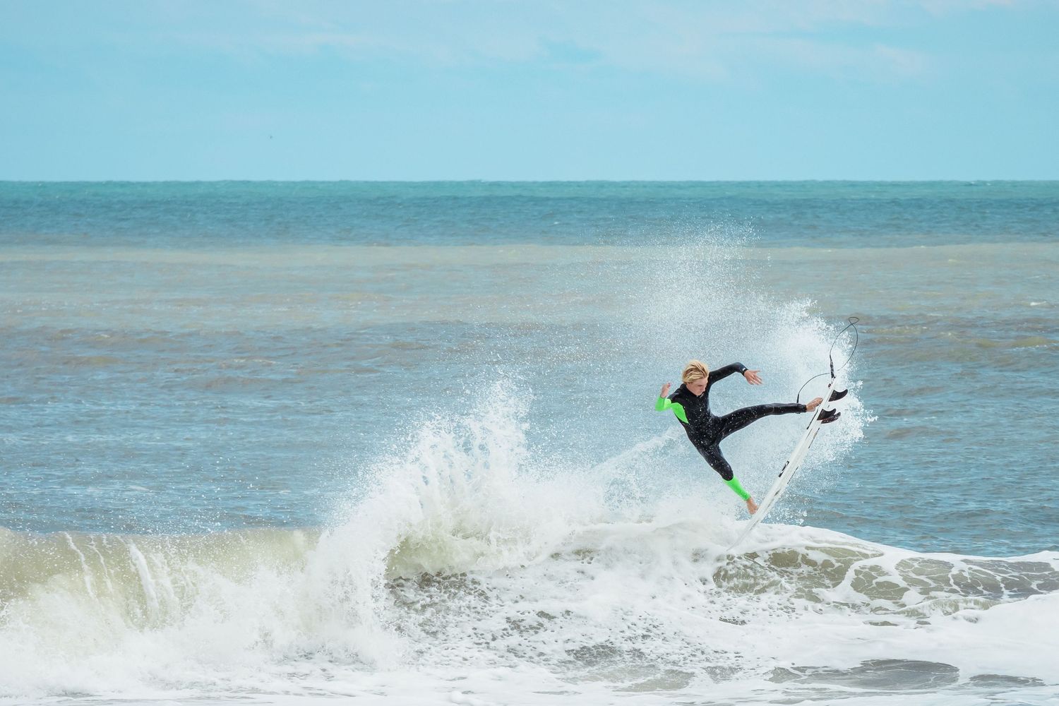 Surfer performing ana air reverse above breaking ocean waves against blue sky in Wrightsville Beach, NC