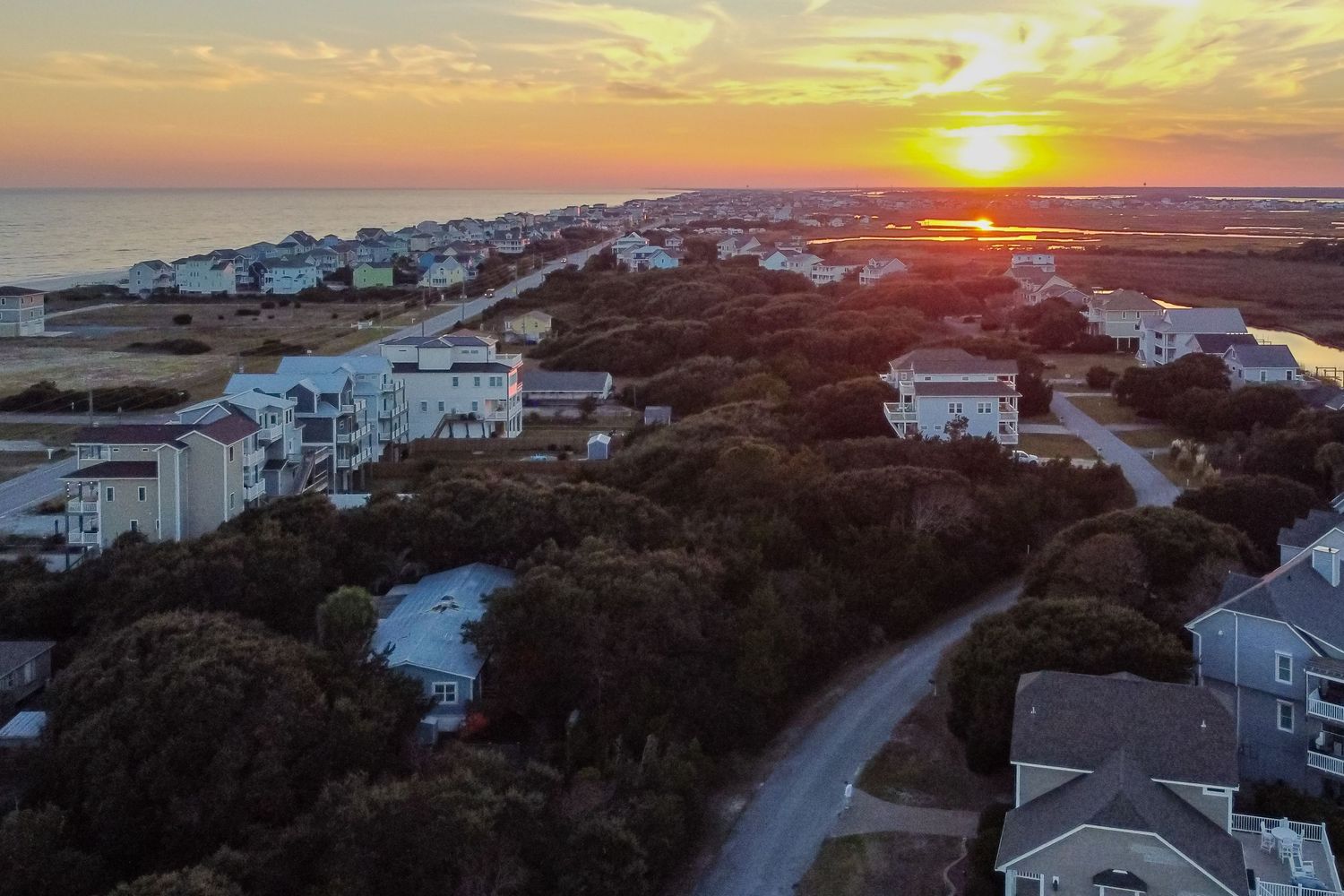 Aerial sunset view over a coastal town with homes nestled among trees near the ocean shoreline.