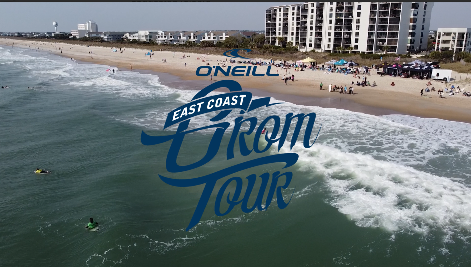 Aerial view of O'Neill East Coast Grom Tour surfing competition on a sandy beach with ocean waves.