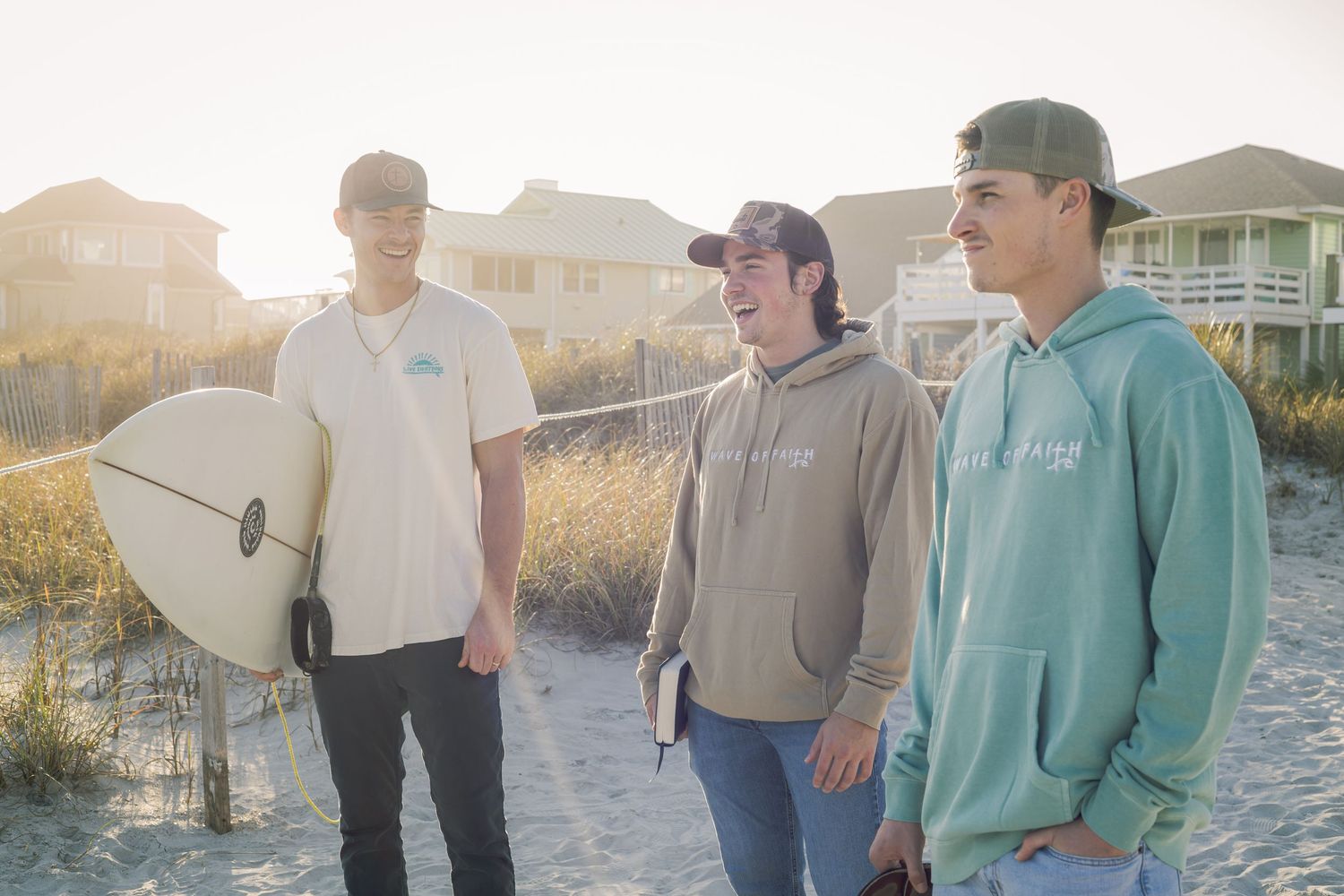 Group of surfers standing on beach dunes during golden hour.