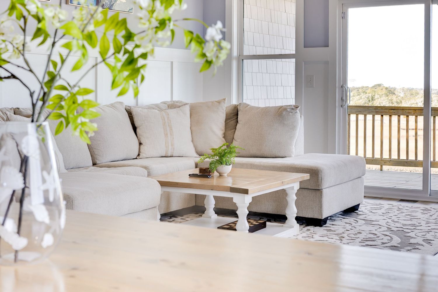 Bright living room with white sectional sofa, rustic coffee table, patterned rug, and sliding doors to a sunny deck.