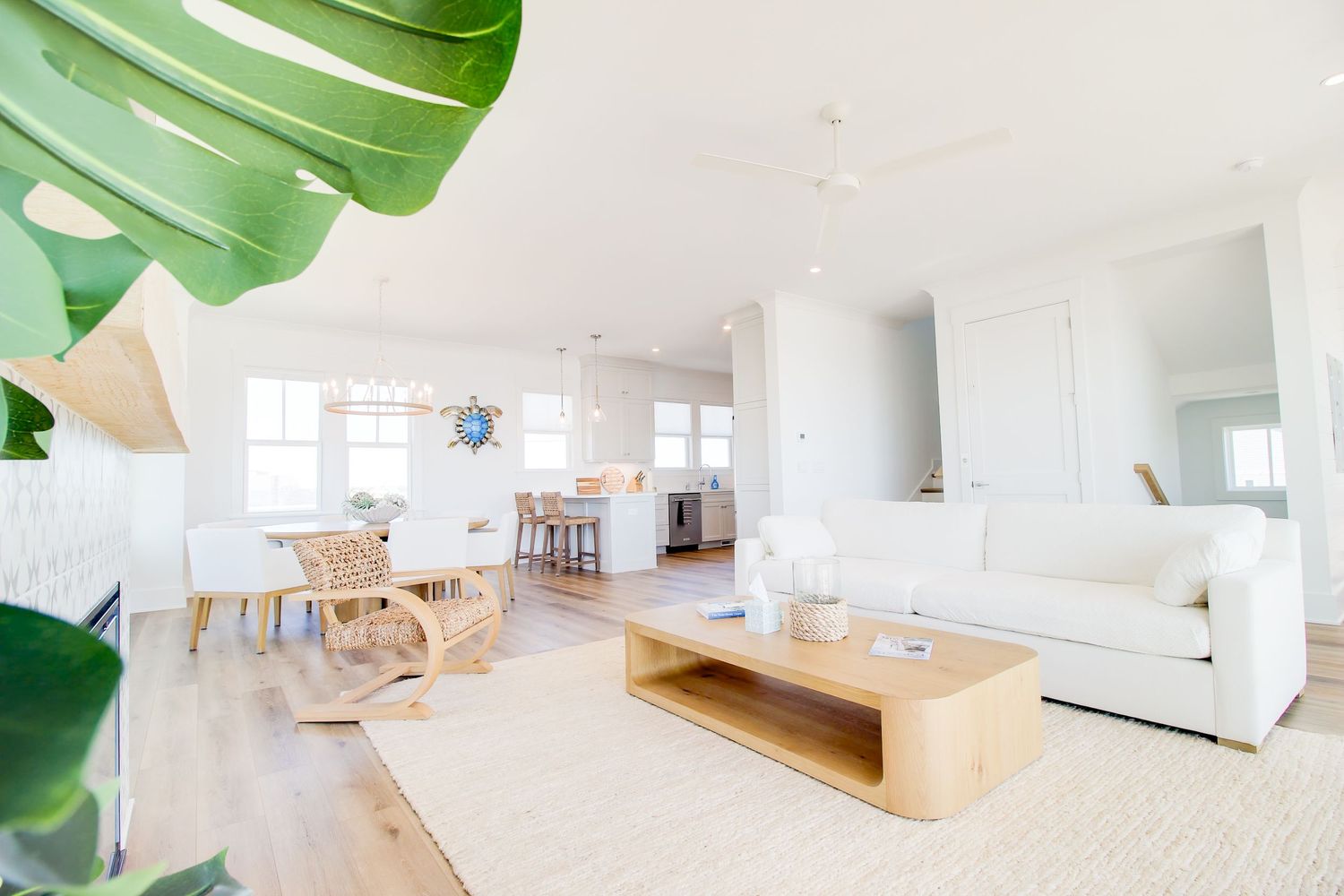 Bright open-plan living room with white sofa, wood coffee table, jute rug, and modern kitchen in coastal style.