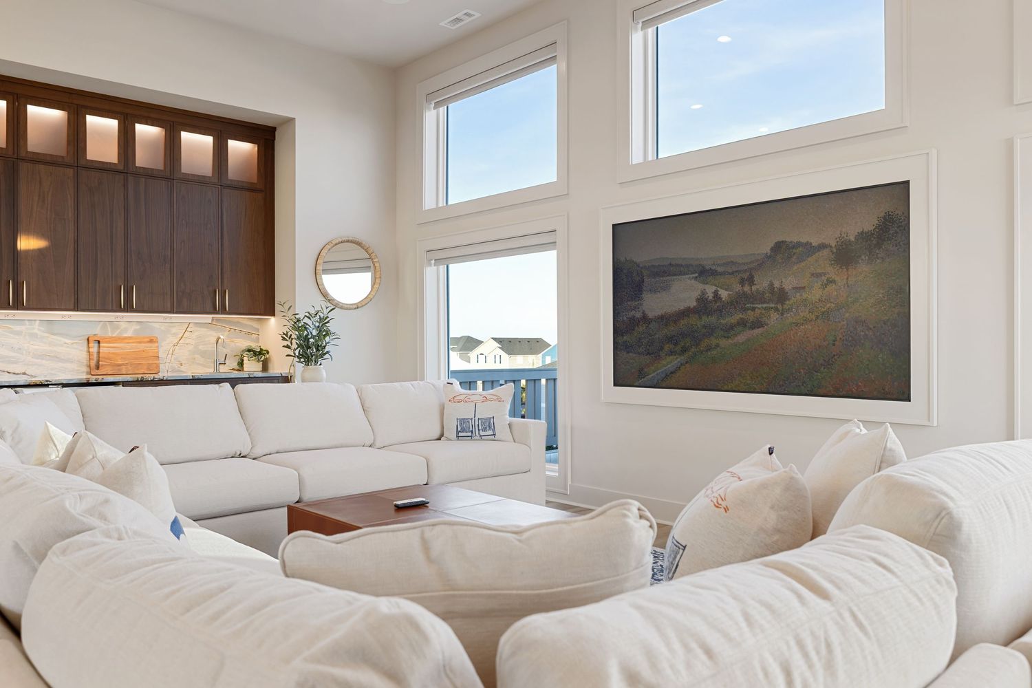 Bright living room with white sectional sofa, large windows, dark wood built-ins, and a landscape painting on the wall.