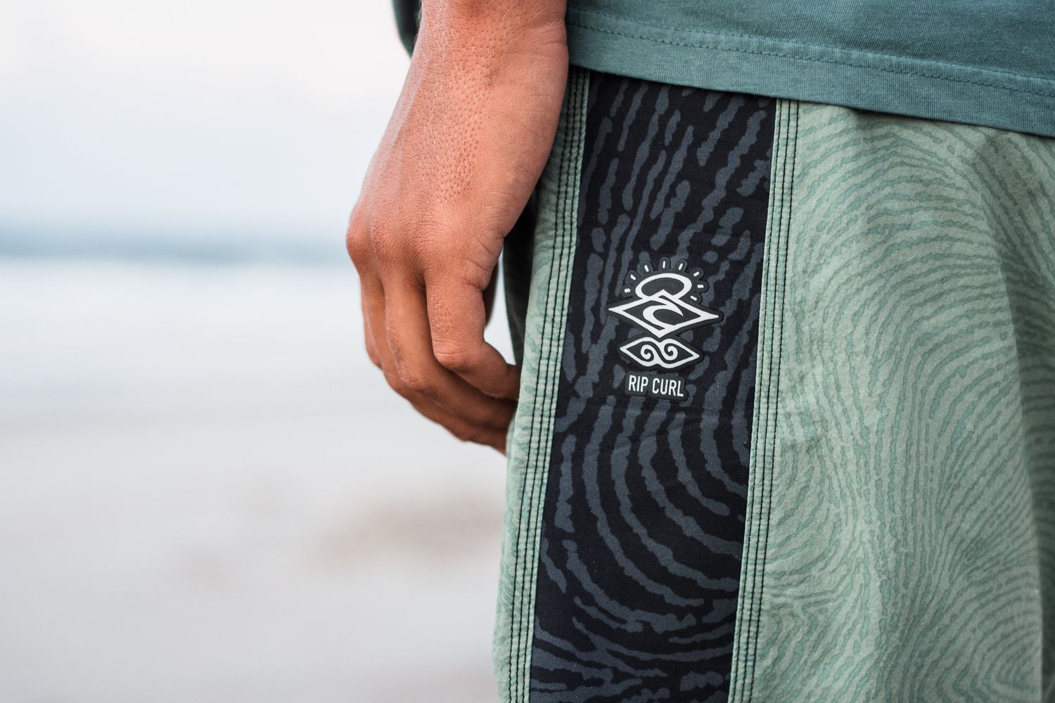 Close-up of surf brand logo on teal colored beach shorts.