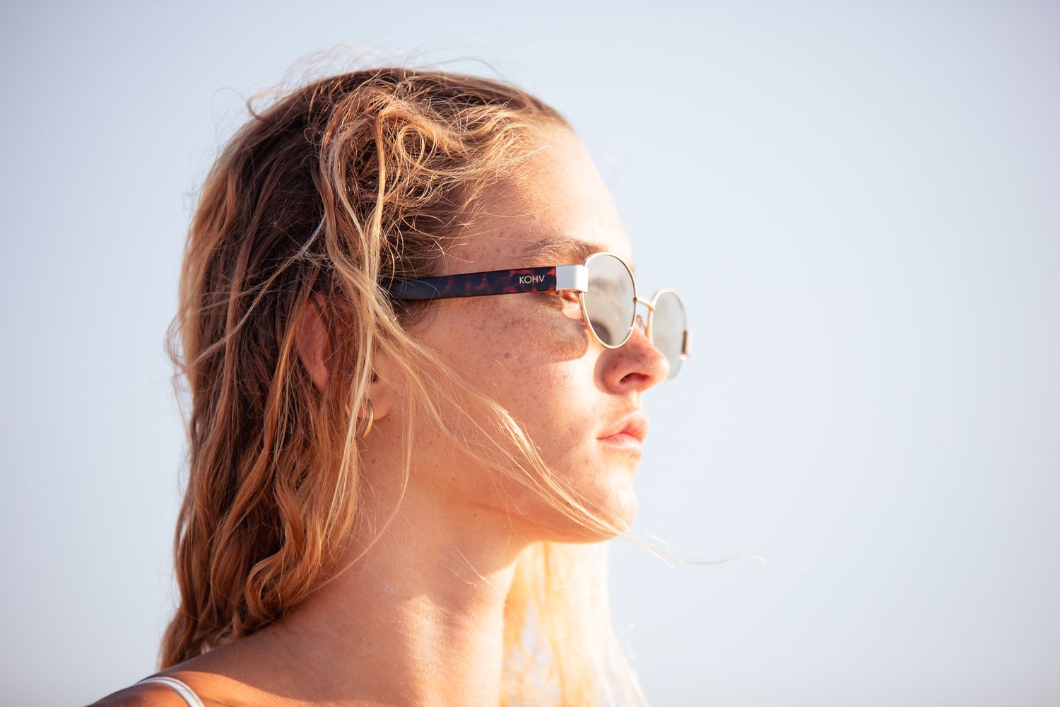 Young woman with blonde hair wearing stylish sunglasses outdoors against a clear sky on a sunny day.