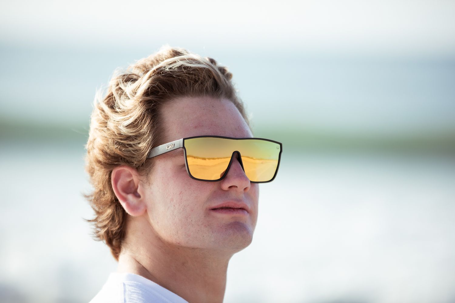 Modern reflective sunglasses with orange lenses against an ocean backdrop.