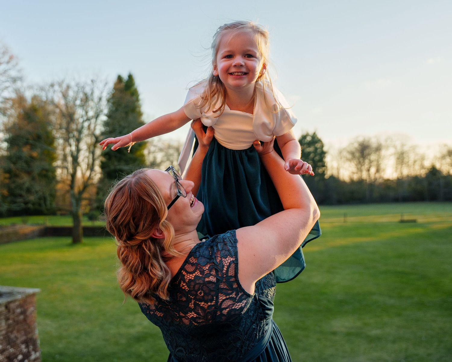 A young woman holds a child up in the air. Child showing joy on her face with arms outstretched