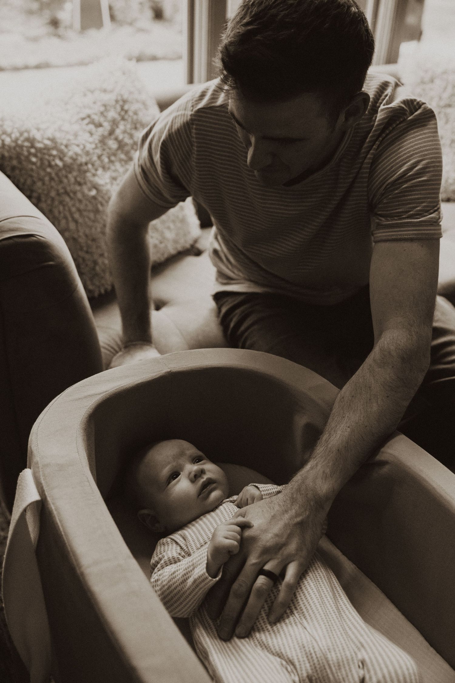 Caring father in sepia photo gently placing hand on newborn baby lying in bassinet.