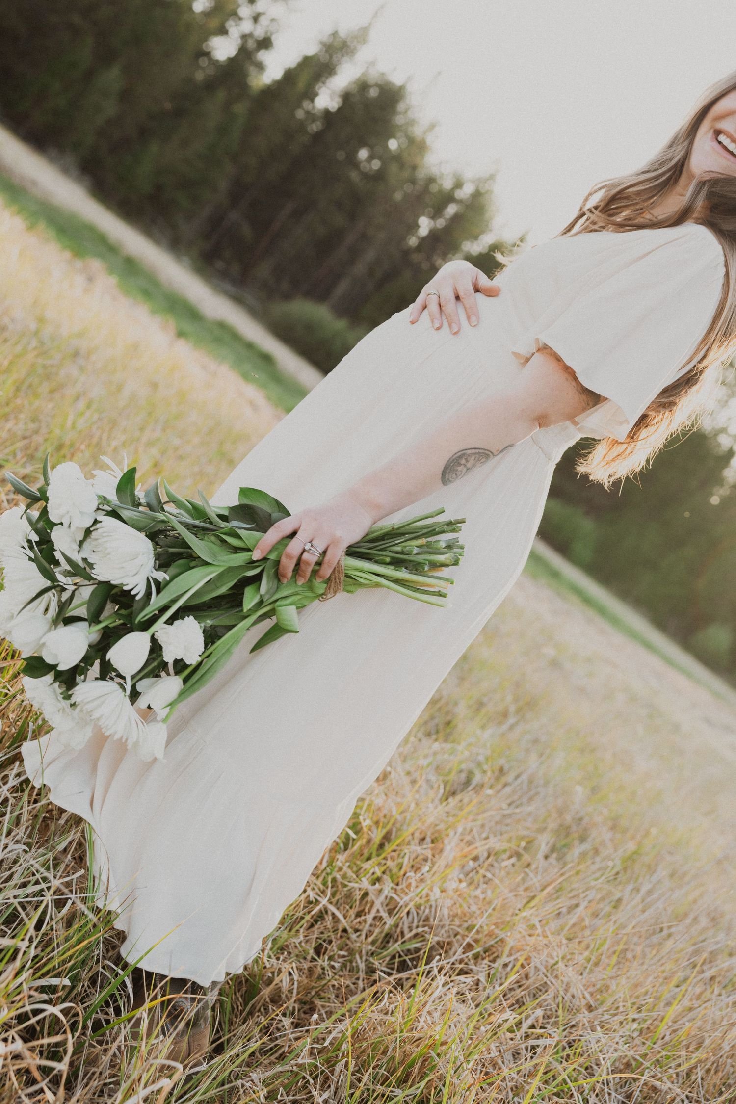 Woman in white dress holding white tulip bouquet in a sunlit field.