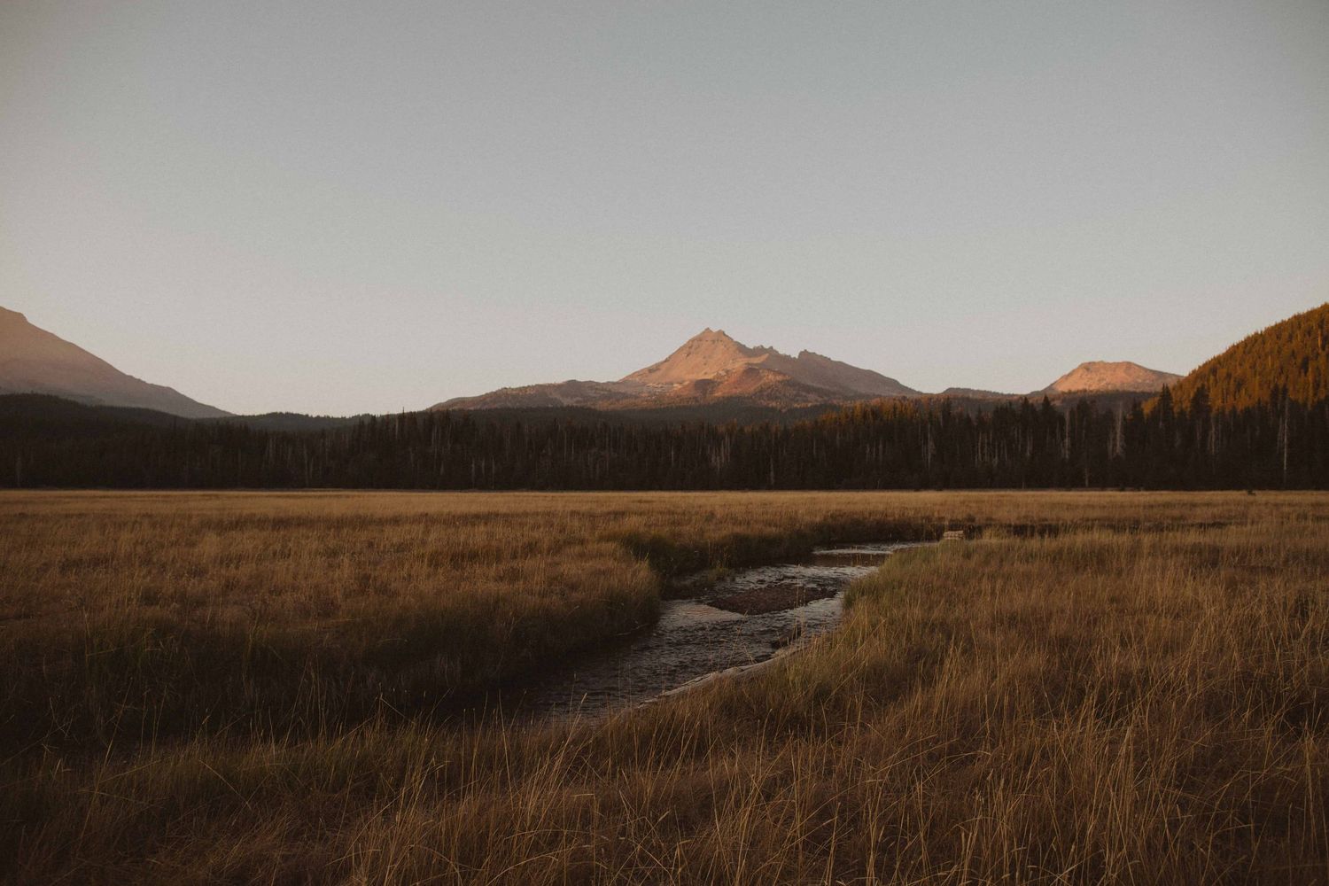 Scenic mountain landscape with winding stream through golden grass at sunset.