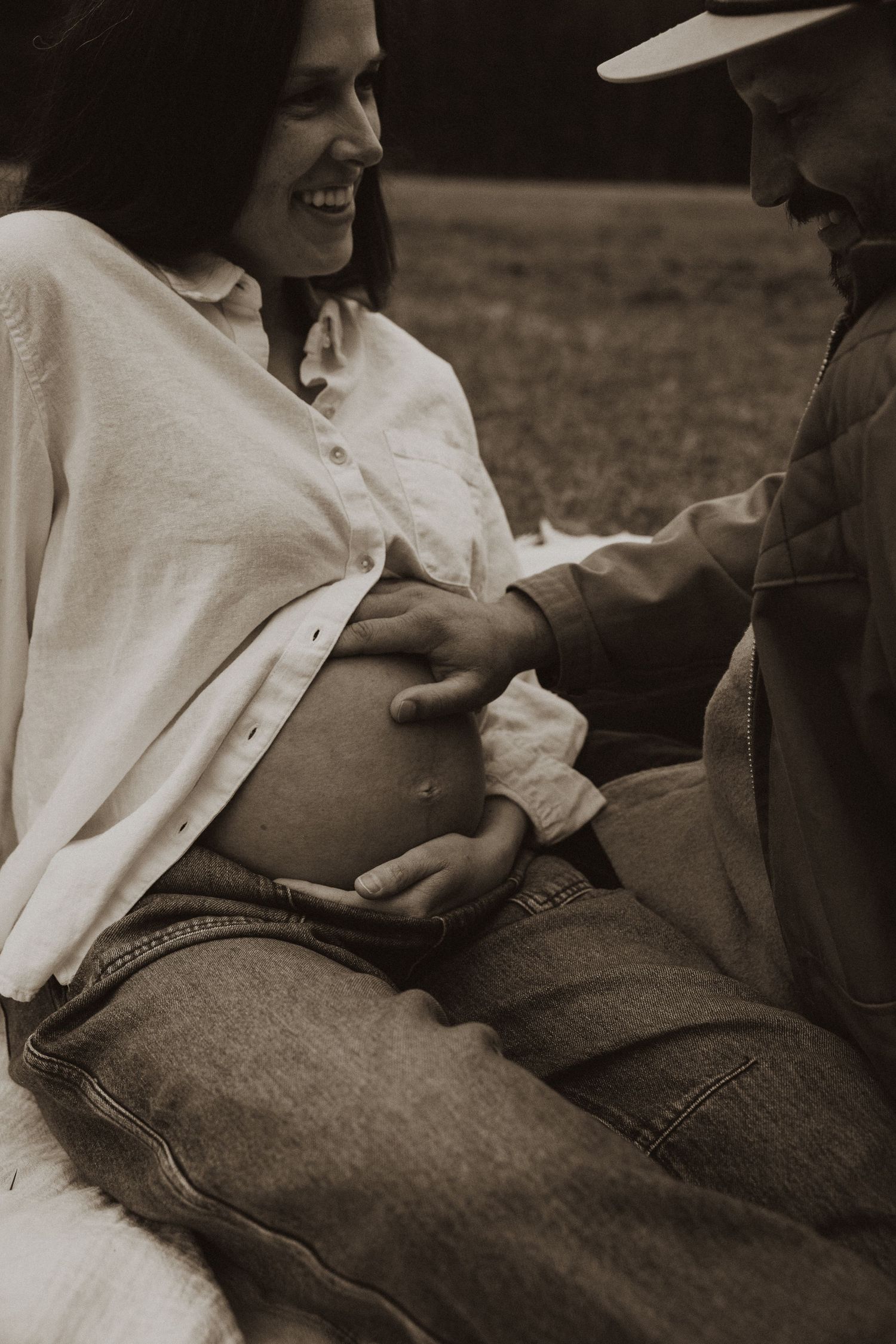Black and white photo of laughing pregnant woman and partner tenderly touching her baby bump.