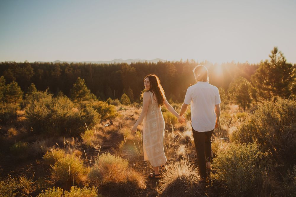 A couple walks hand in hand through a desert landscape at sunset.