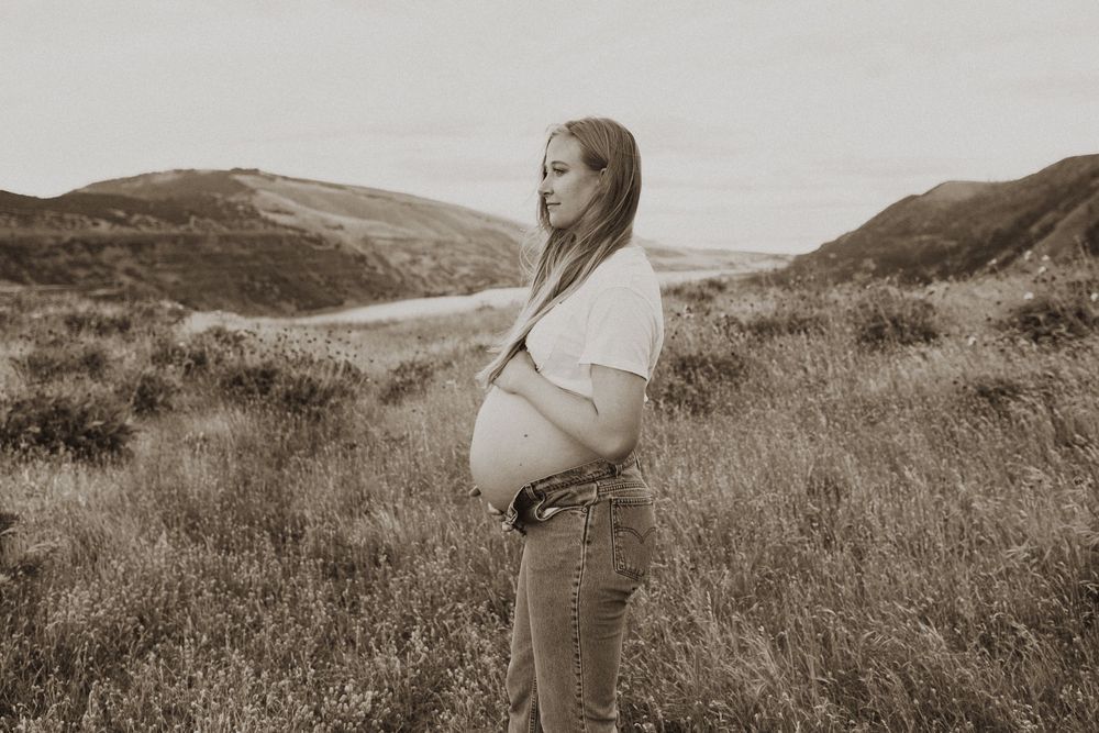 Artistic maternity photography sequence captured in a rustic outdoor hillside setting.