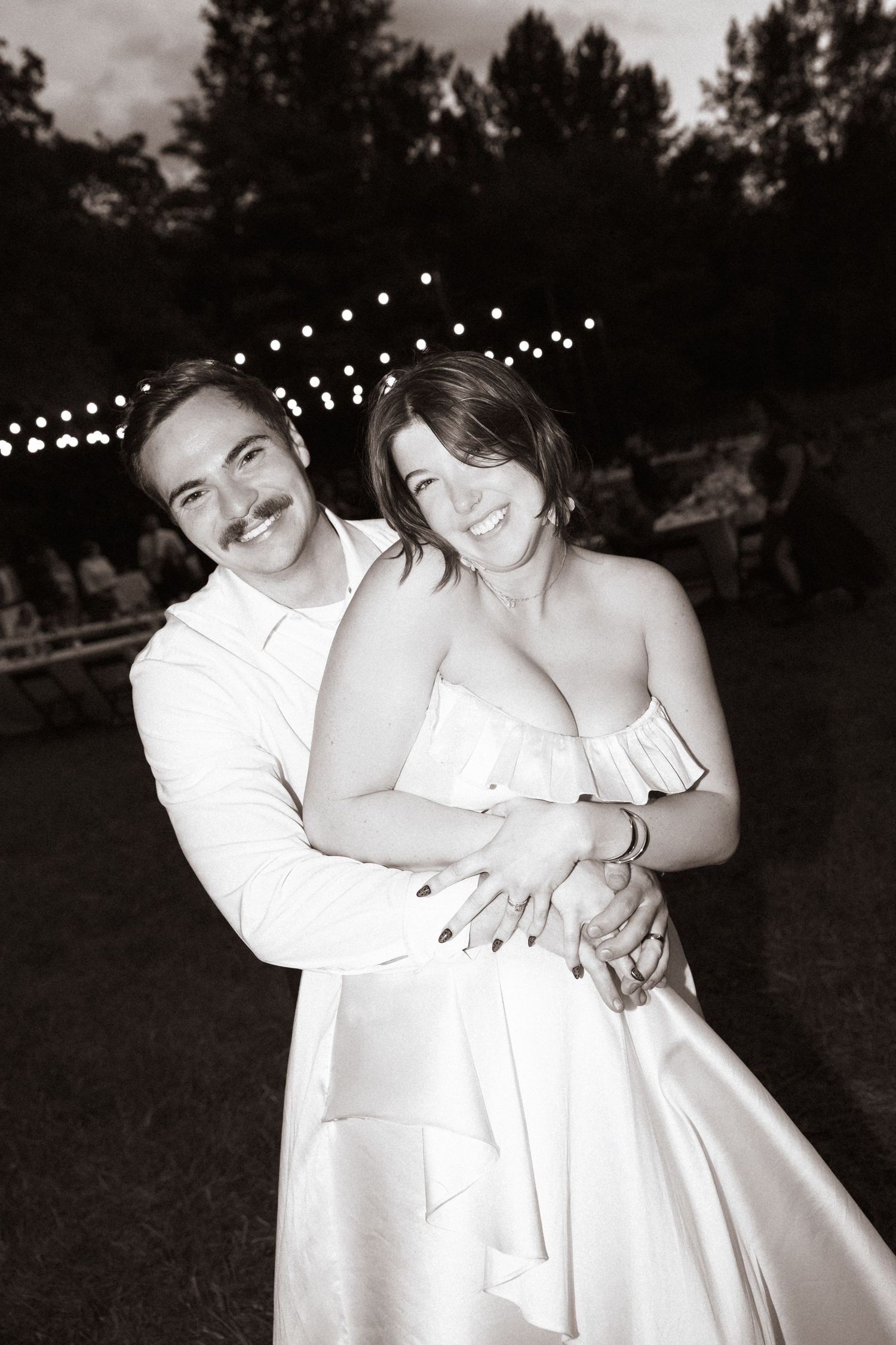Bride and groom embracing and smiling during outdoor wedding reception at night.