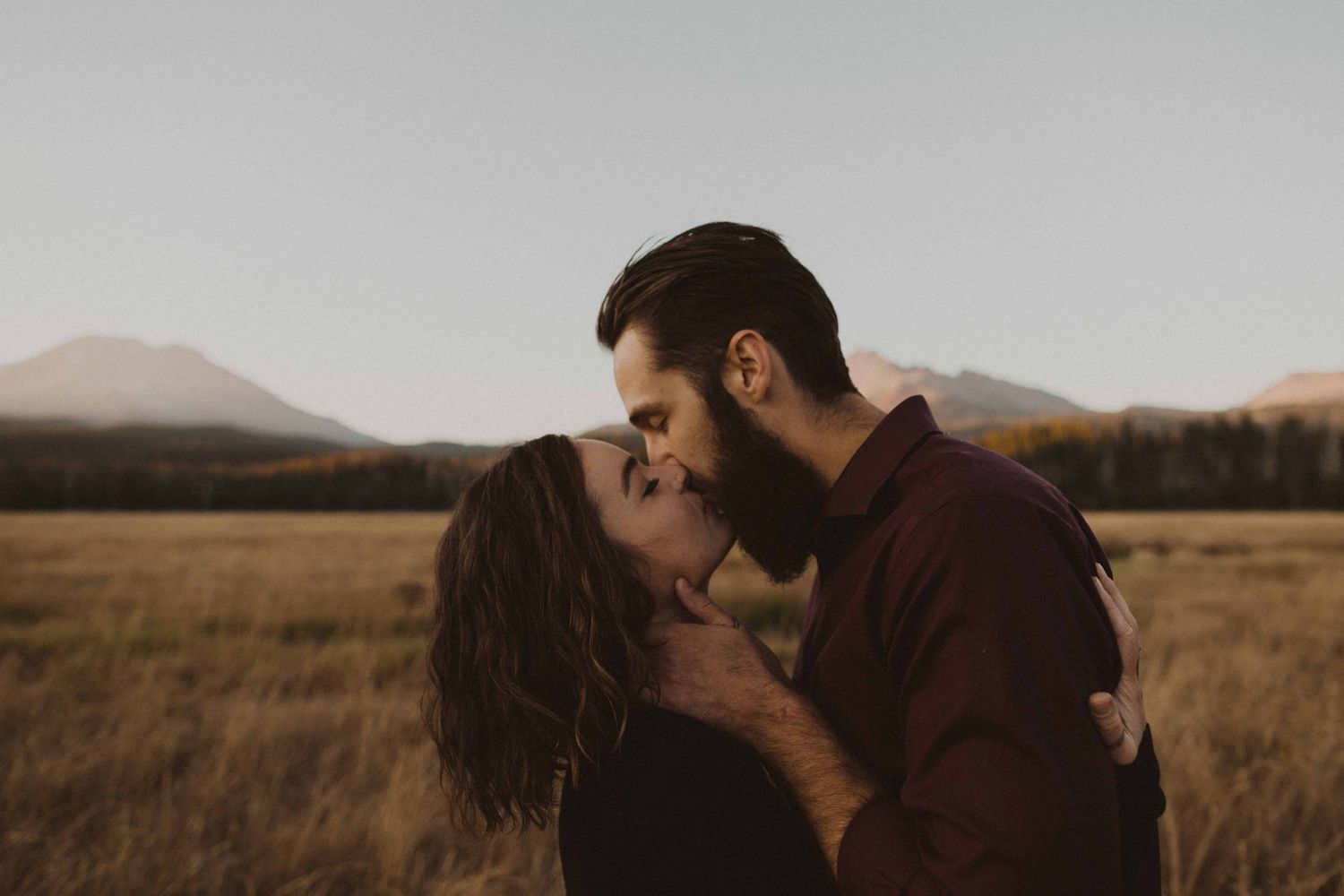 Intimate moments captured between two people in a scenic field during golden hour.