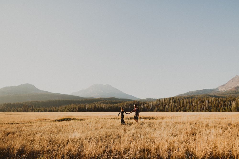 Two silhouettes standing in a vast golden field with mountains in the background.