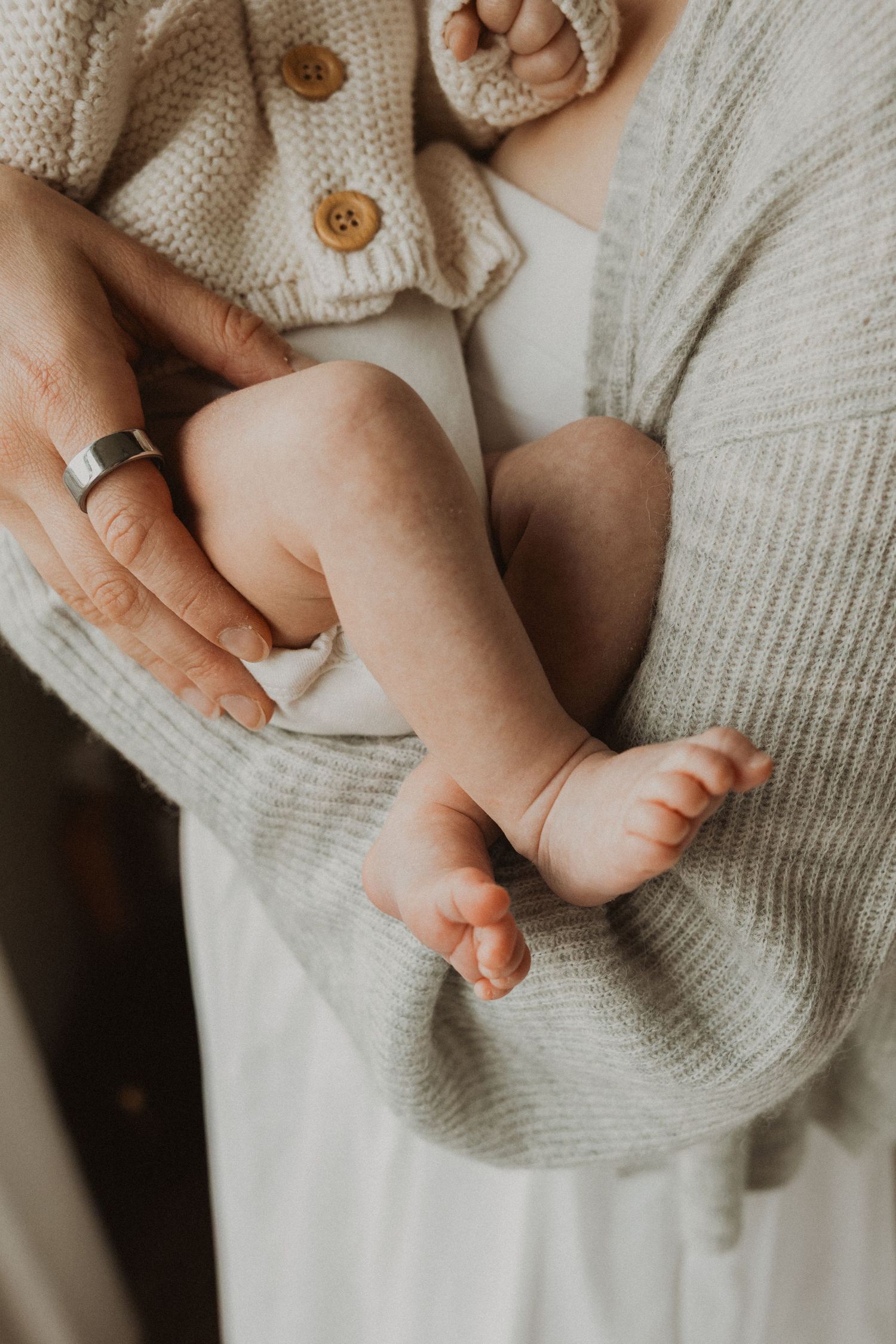 Close-up of a parent holding a newborn baby's tiny bare feet and legs, wearing a cozy knit cardigan.