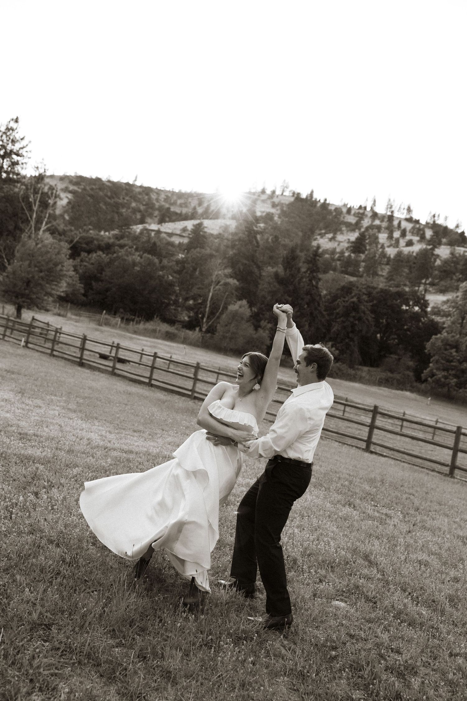 Bride and groom dancing joyfully in a scenic countryside field on their wedding day.