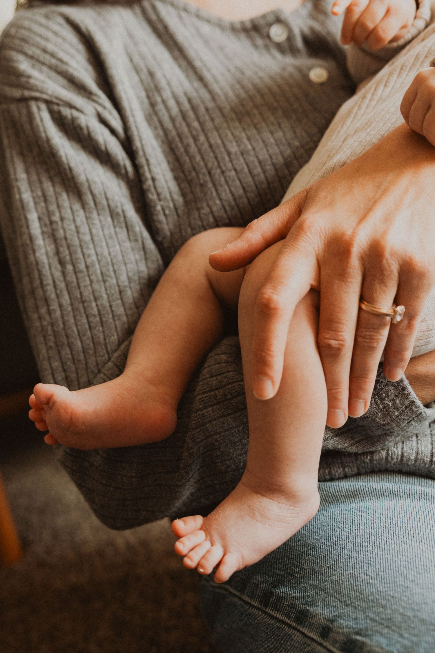 Close-up of a parent cradling a newborn baby's tiny feet and legs while wearing a diamond engagement ring.