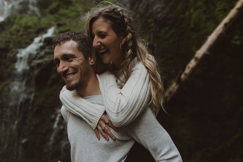 Romantic couple embracing and laughing together near a misty waterfall.