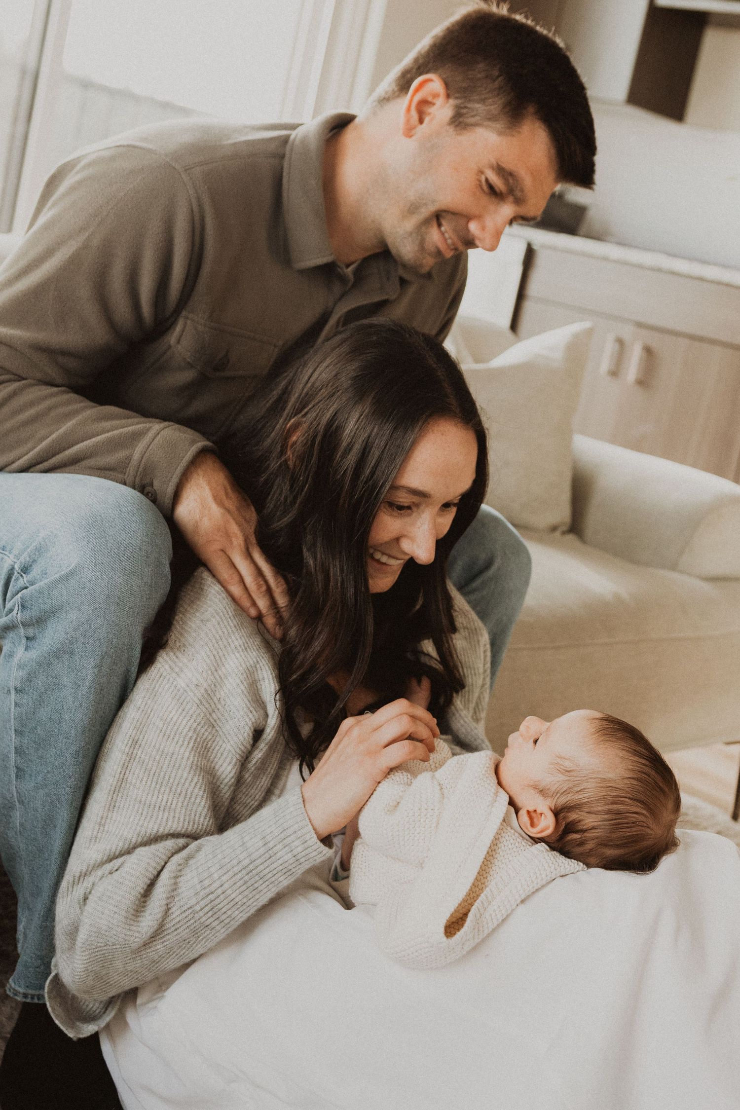 Happy parents smiling at their newborn baby lying in a bassinet during a warm indoor family photo session.