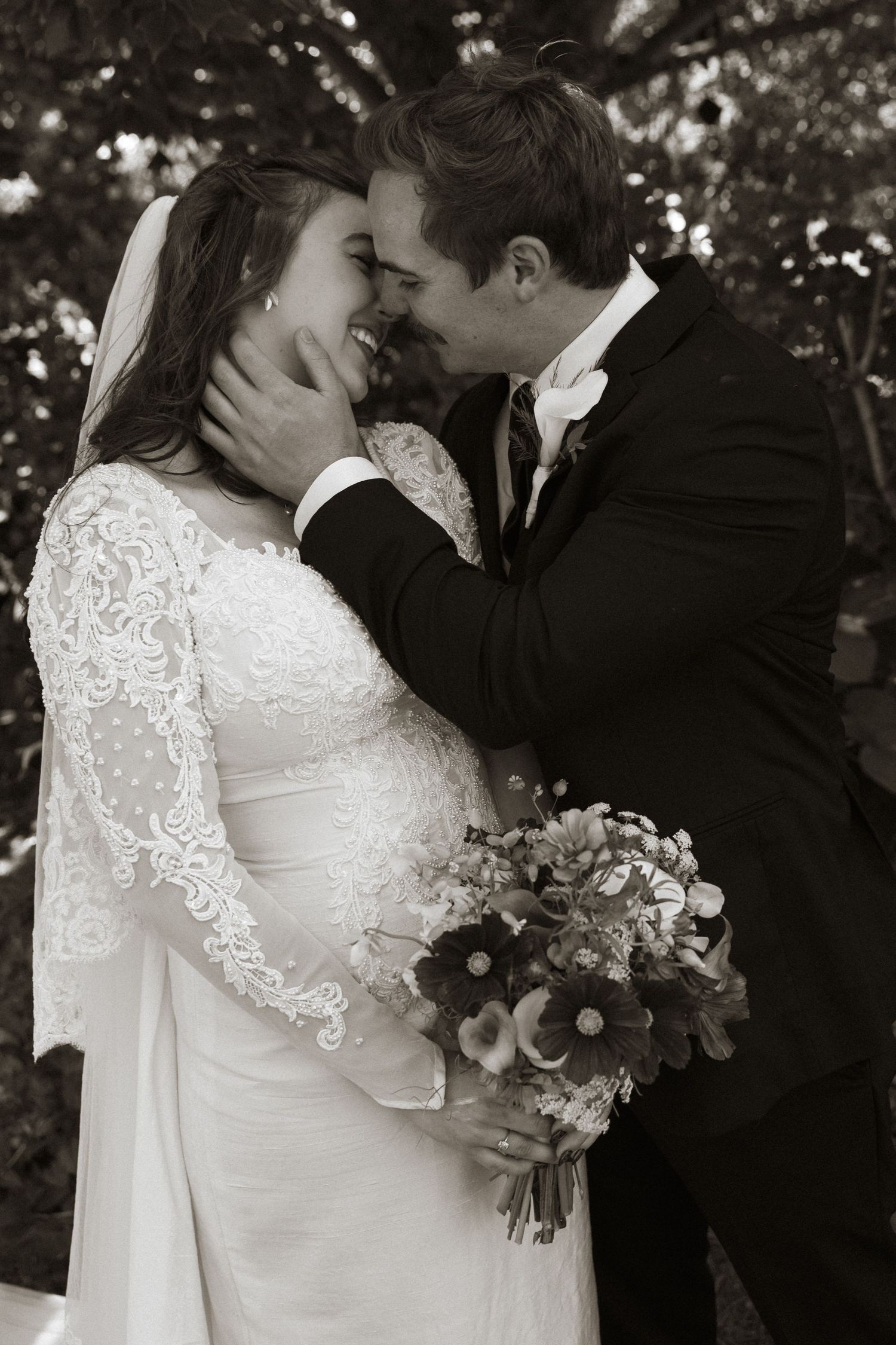 Black and white photo of a bride and groom sharing a romantic moment, bride holding a bouquet of flowers.
