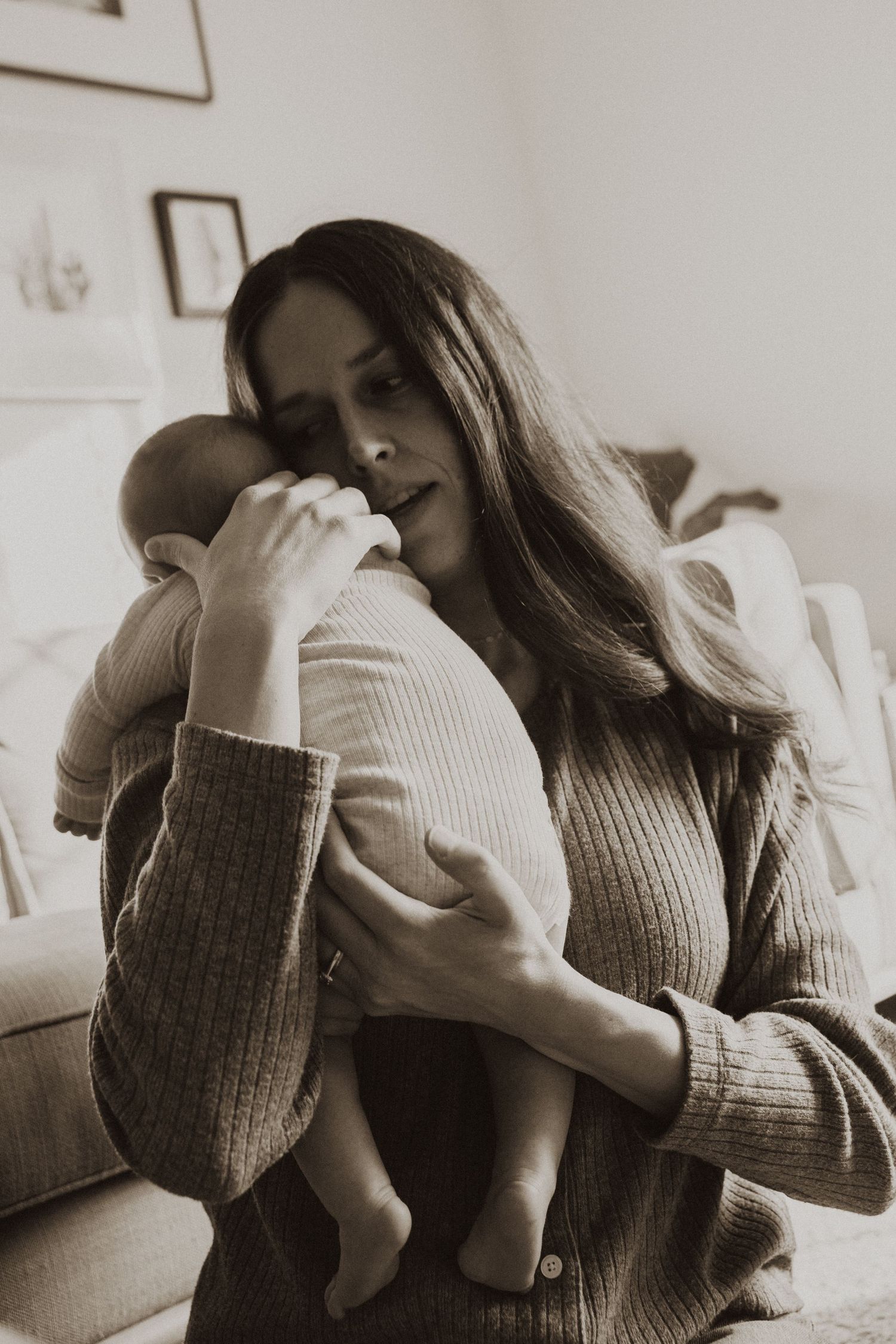 Mother tenderly holding newborn baby close to her face in black and white portrait photo.