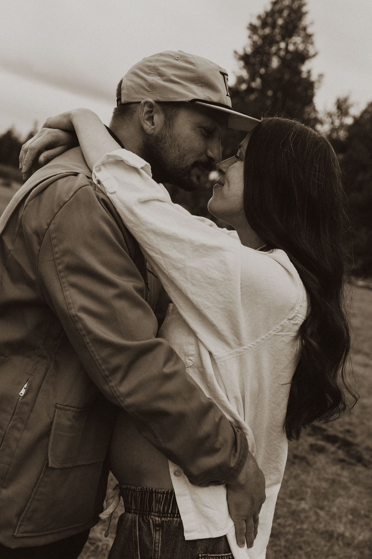 Black and white photo of a couple embracing and sharing a tender moment in an outdoor field.