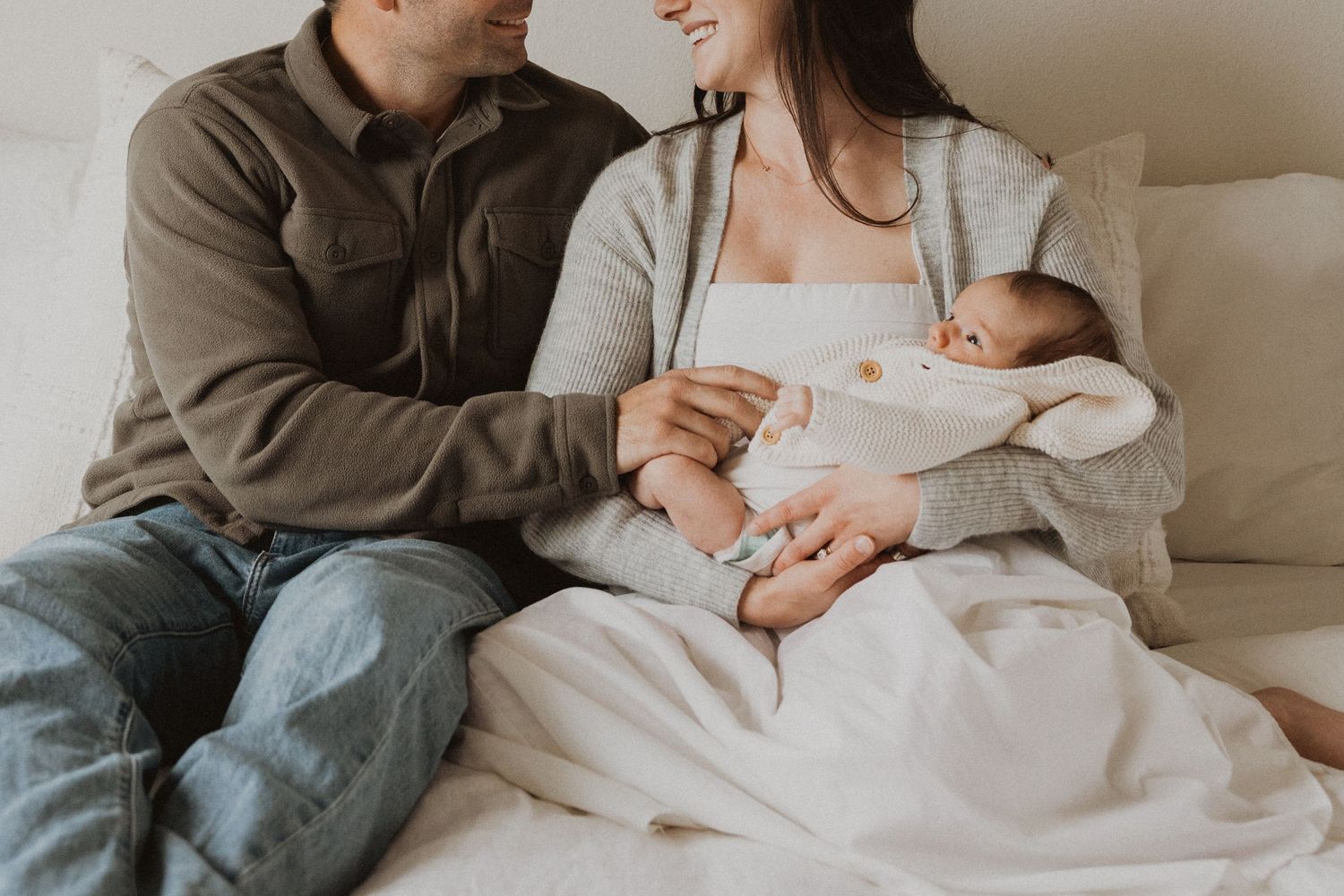 Happy couple sitting on bed holding their newborn baby, sharing a tender family moment together.