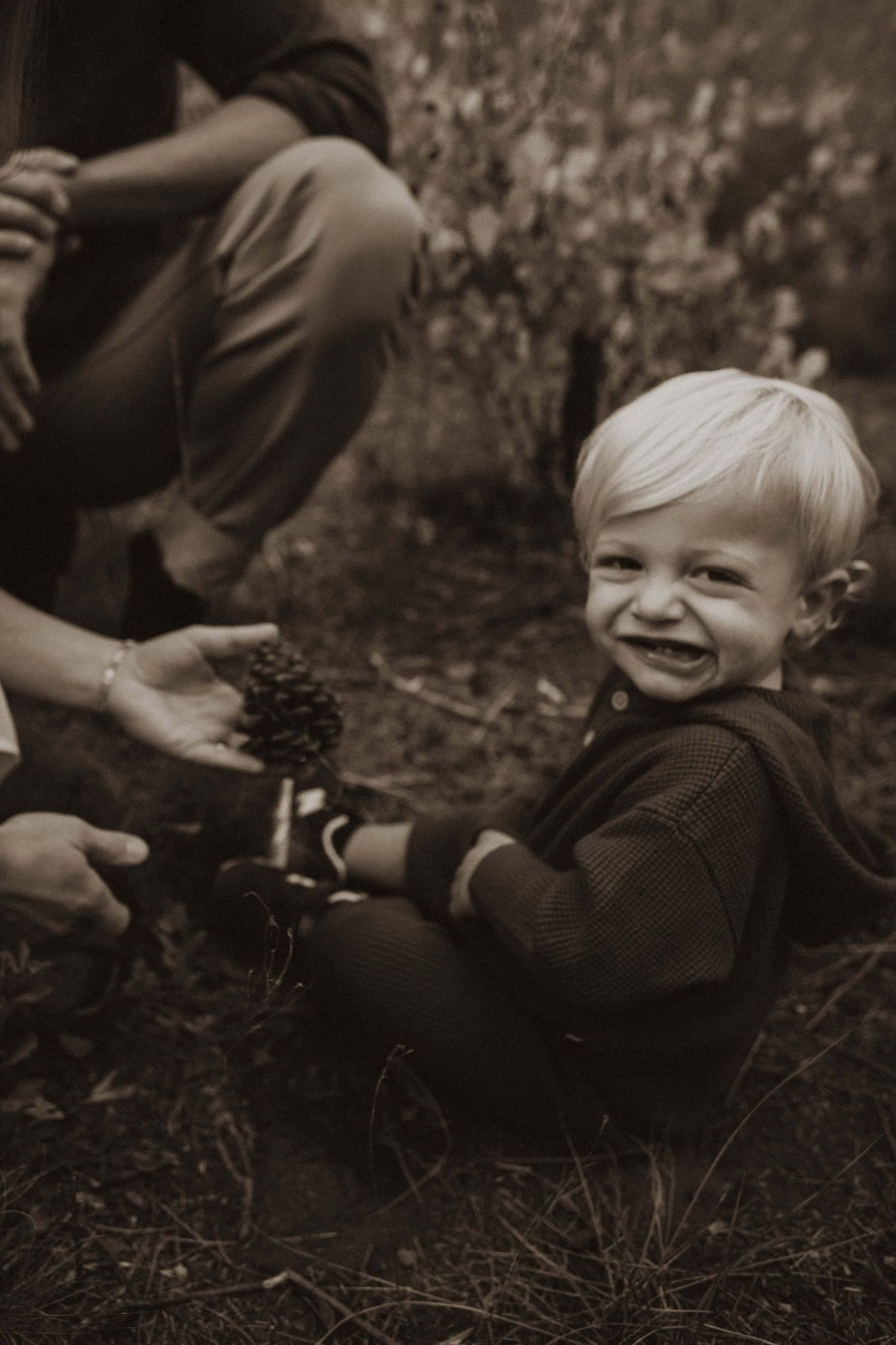 Child playing with pinecones in sepia toned nature photography series.