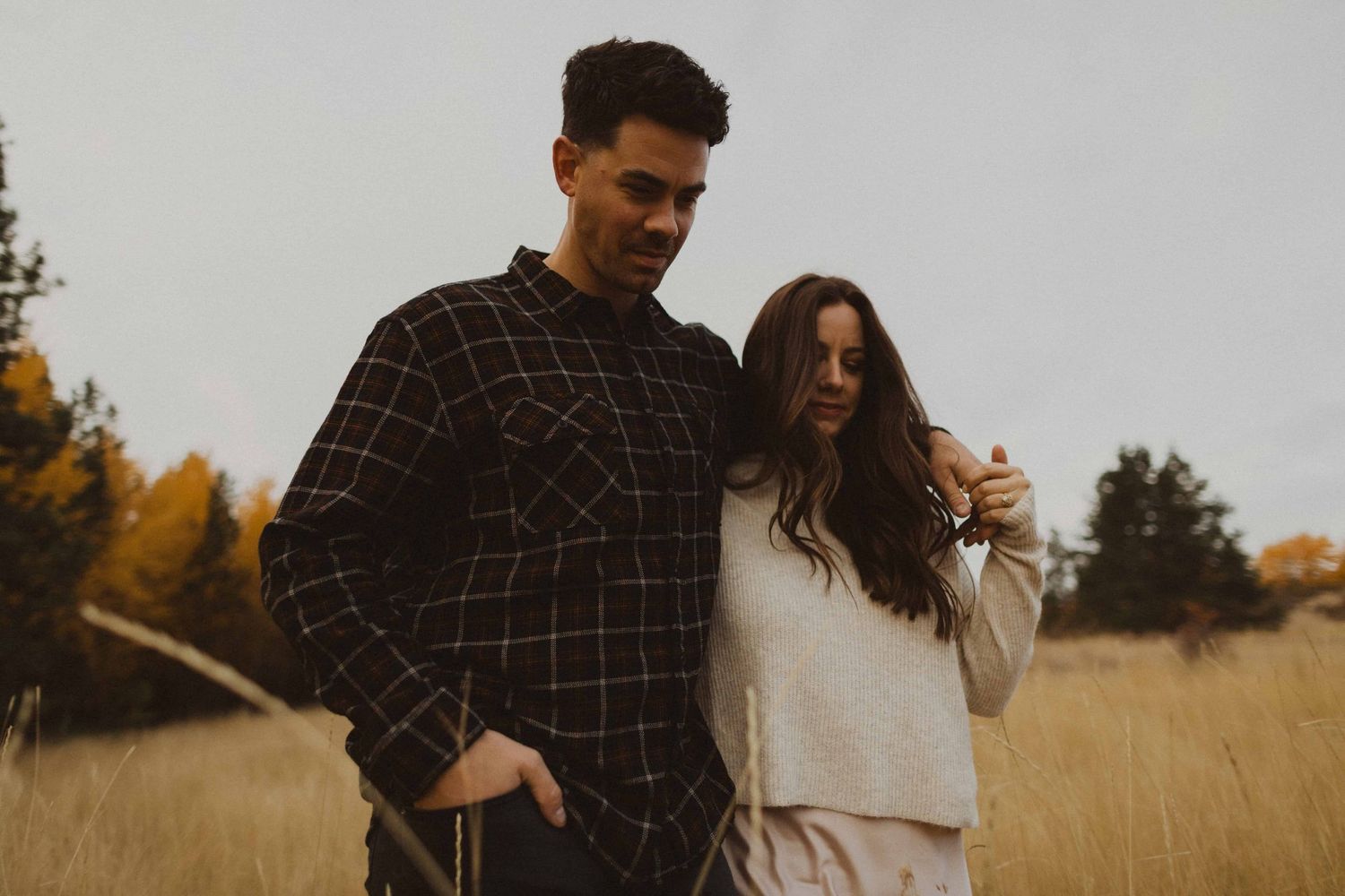 Couple in casual attire sharing romantic moment in autumn field setting.