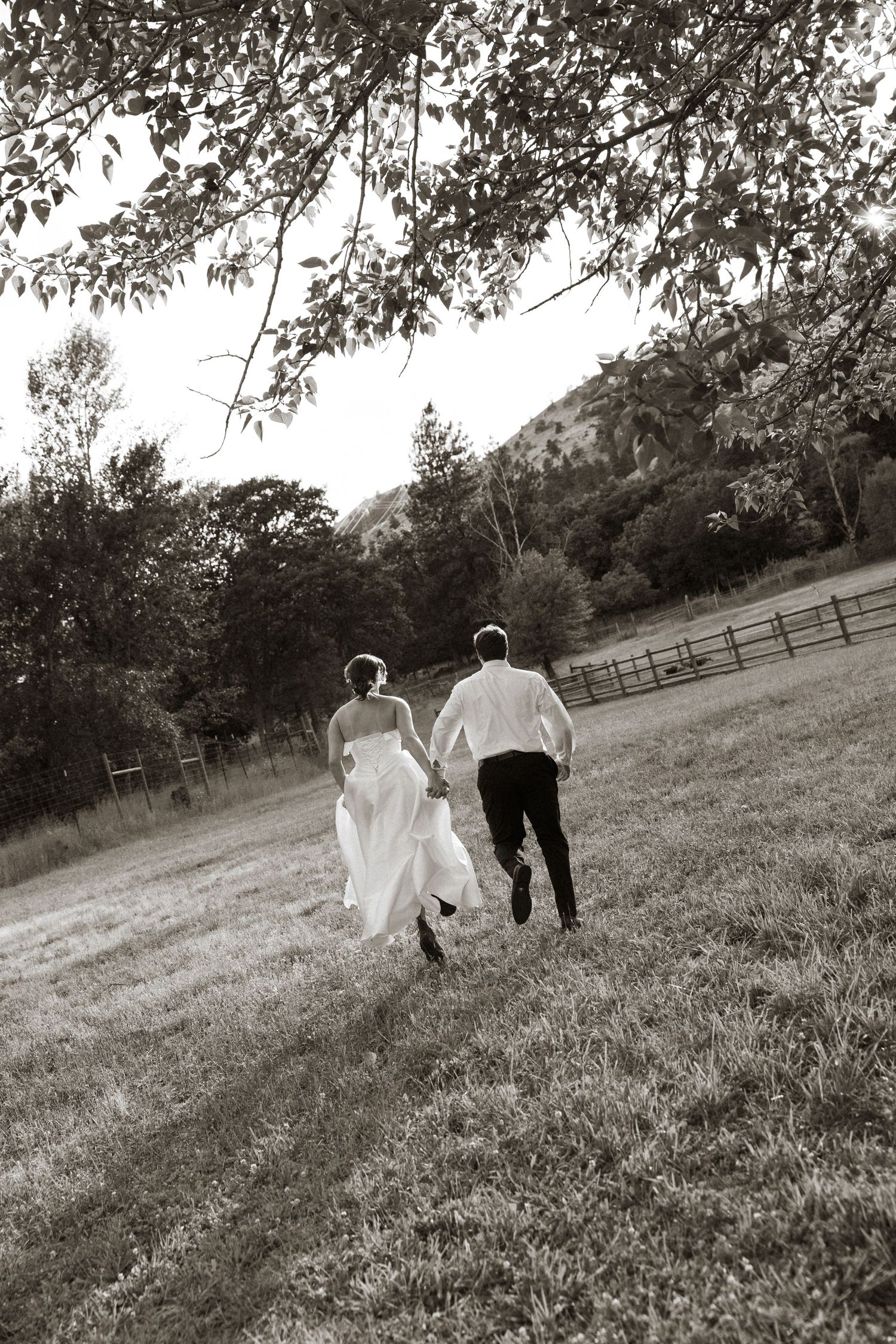 Black and white photo of a bride and groom running hand in hand across an open field.