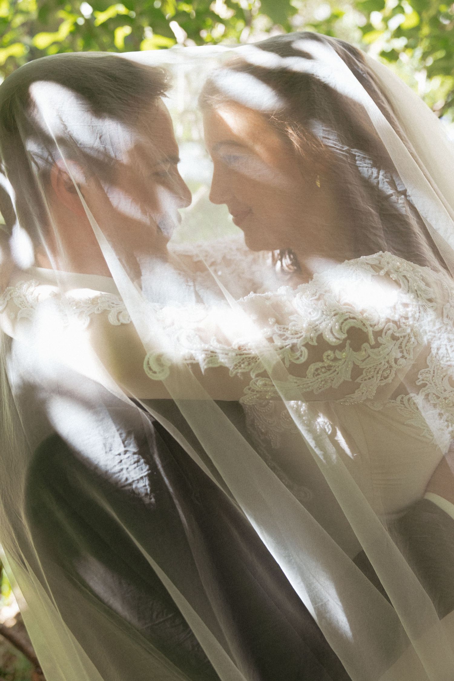 Bride and groom share an intimate moment under a flowing wedding veil outdoors.
