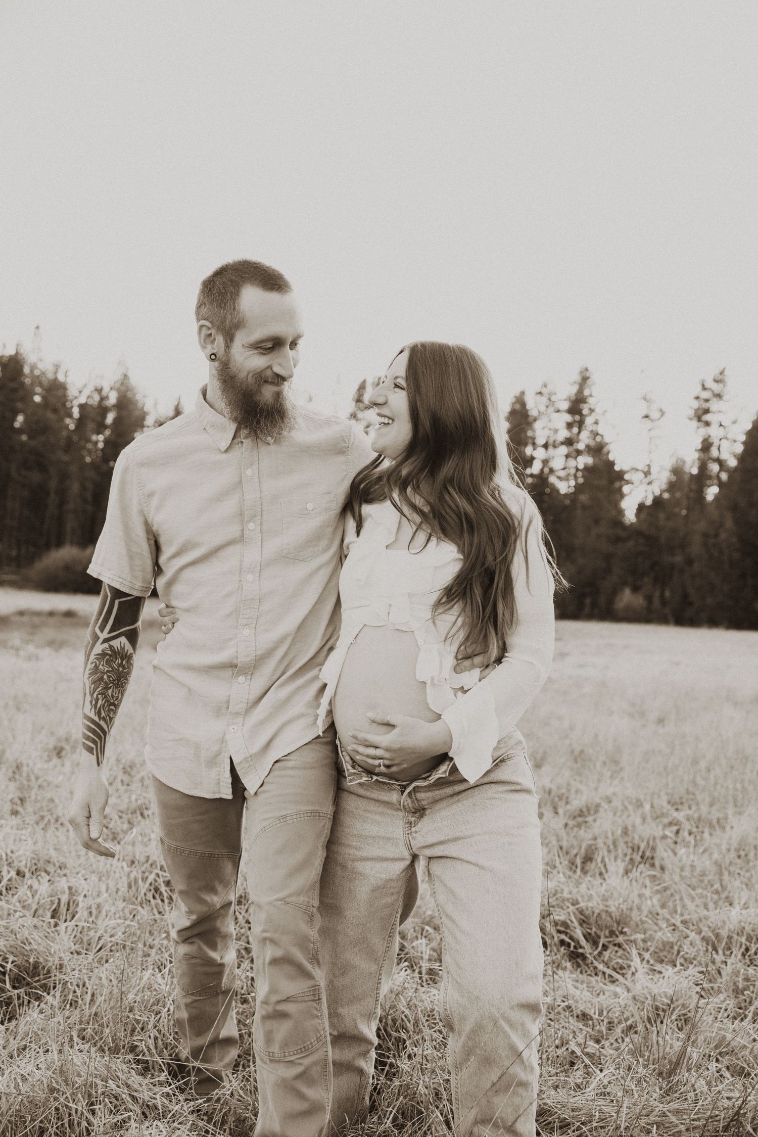 Couple sharing tender moment in field, woman cradling baby bump.