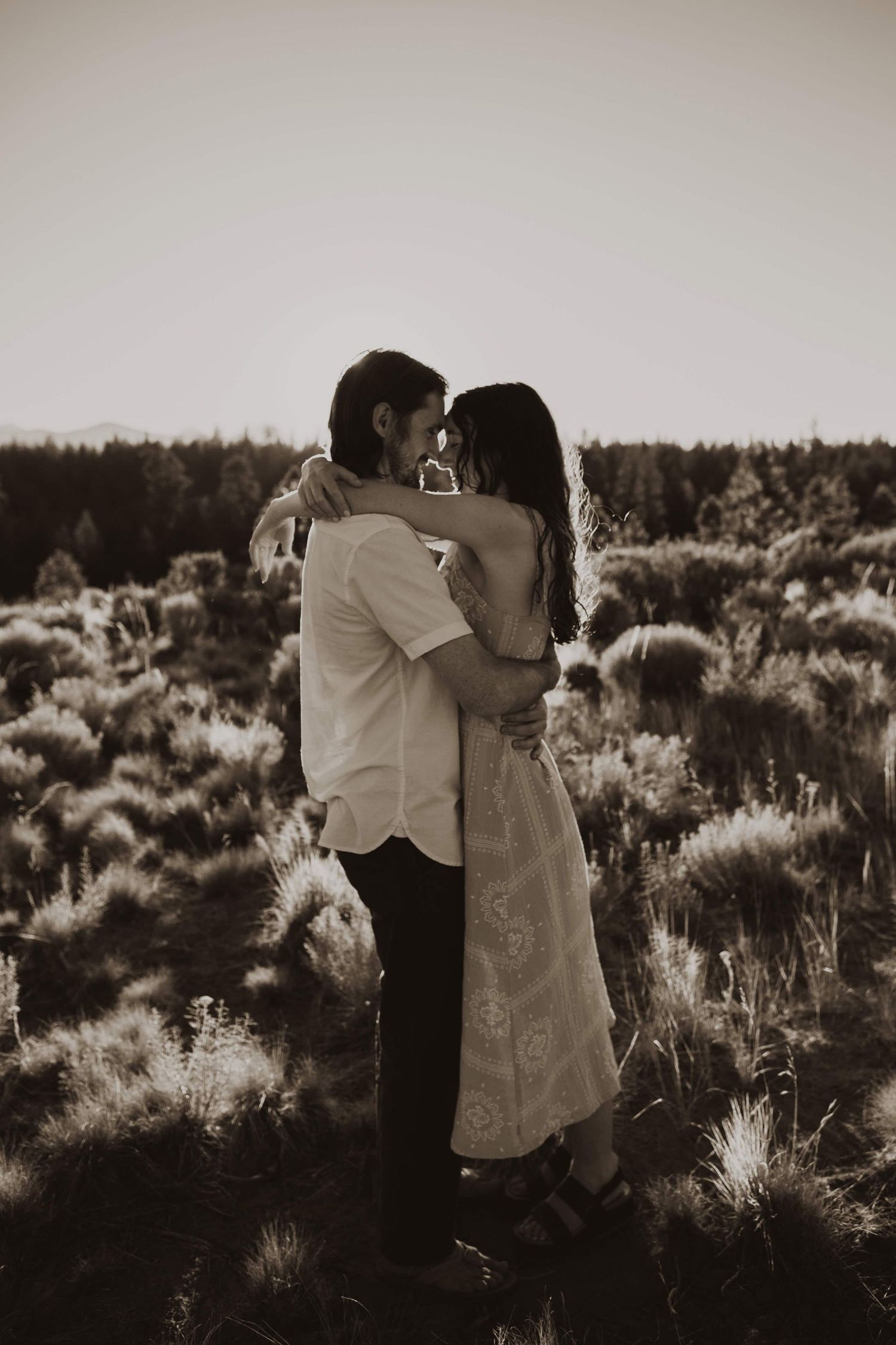 A romantic couple embracing in a desert landscape at sunset.