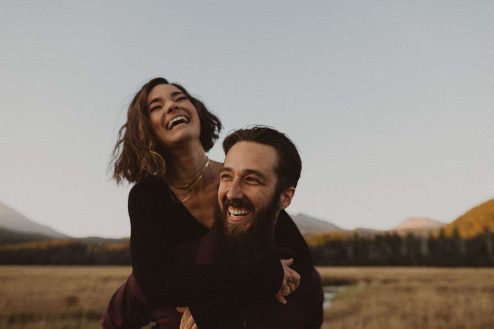 A joyful couple sharing a playful piggyback ride in an autumn field.