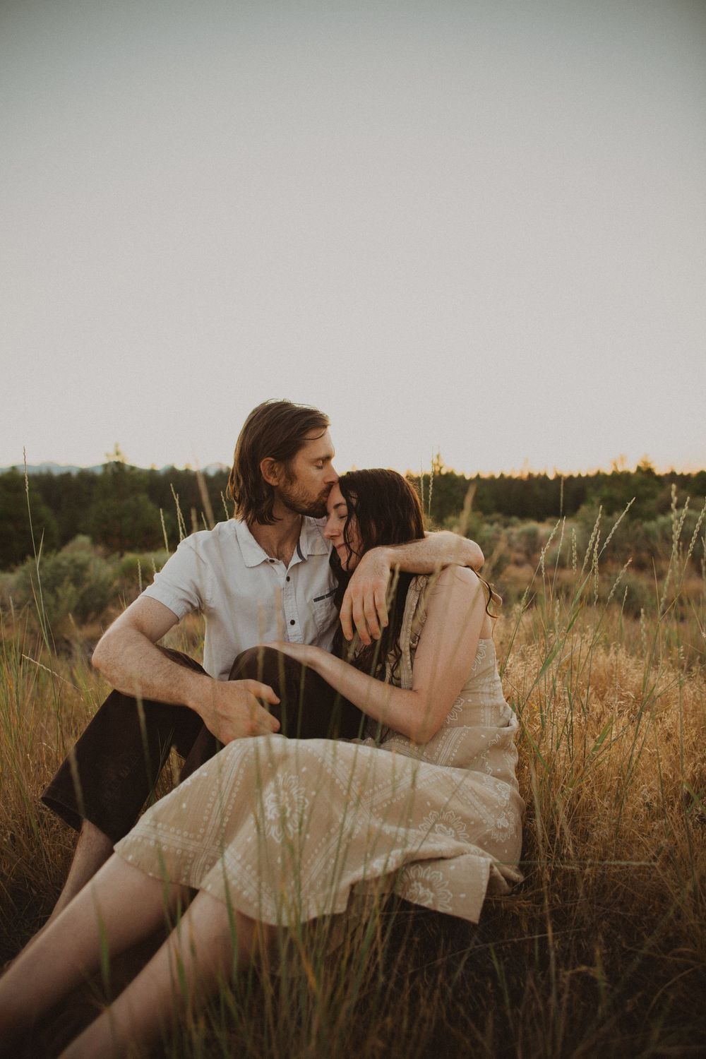 A couple relaxes in tall grass during a romantic outdoor photoshoot.