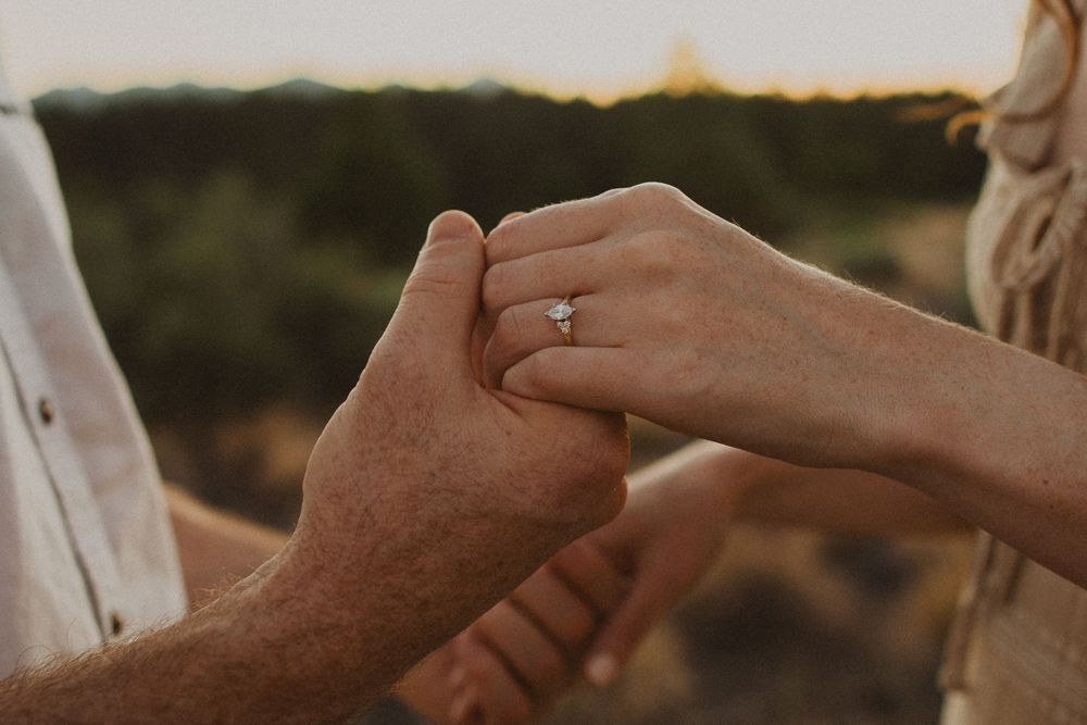 Close-up of hands with engagement ring intertwined in warm sunlight.