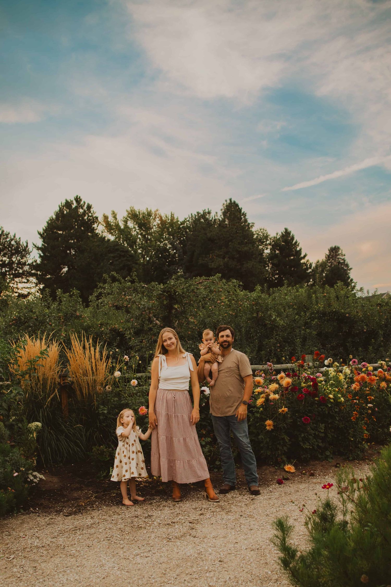 A family poses together on a gravel path surrounded by colorful summer flowers and greenery.