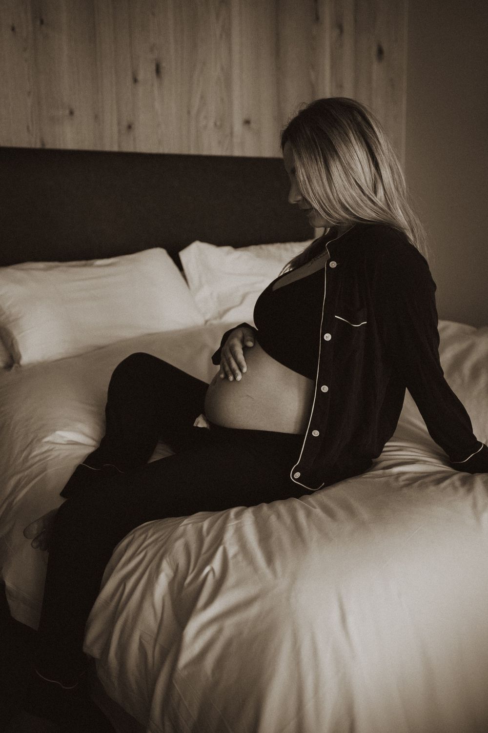 Woman in black outfit lying on white bed sheets in moody boudoir style.