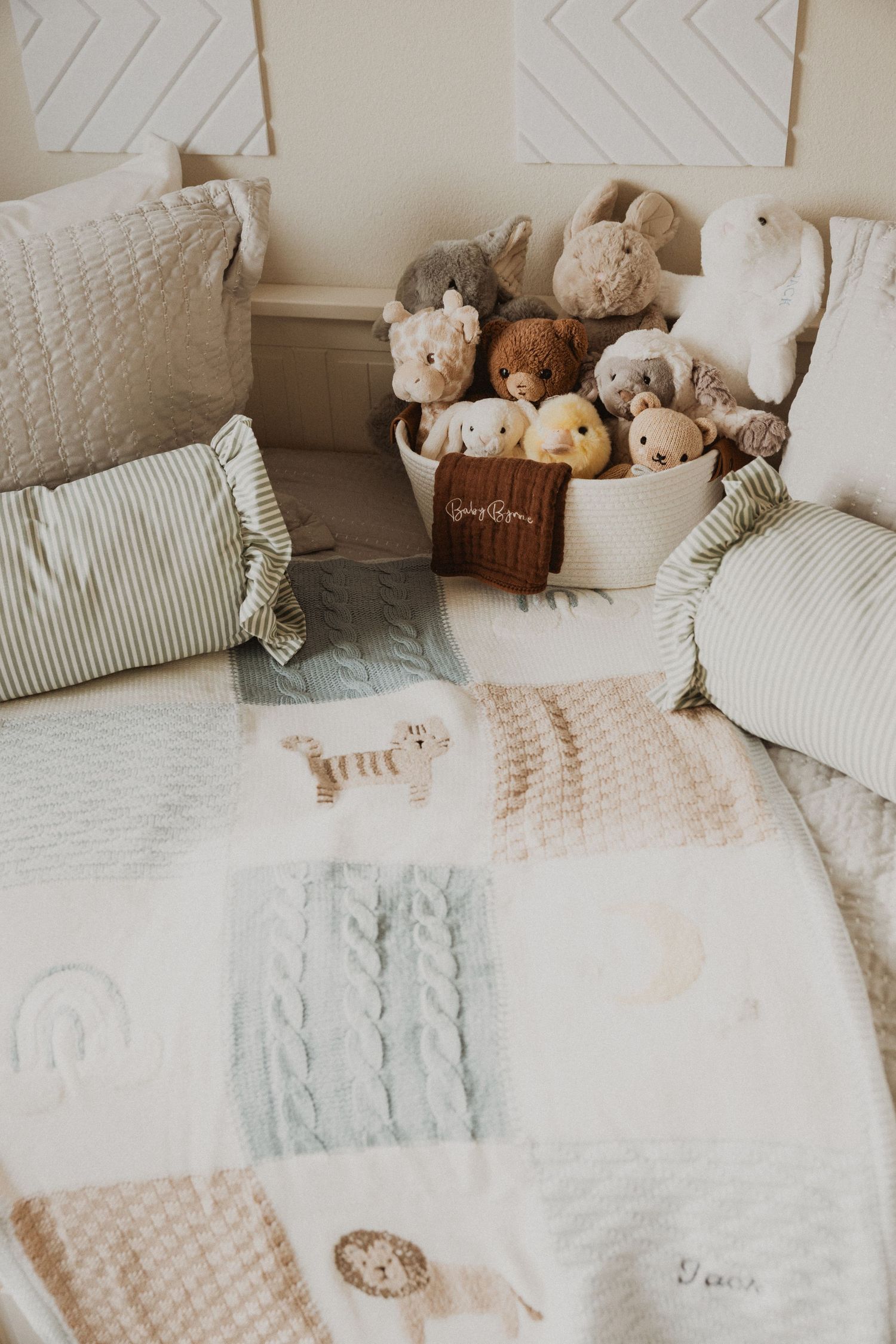 Soft nursery bed with patchwork animal blanket, striped pillows, and a basket filled with plush stuffed animals.