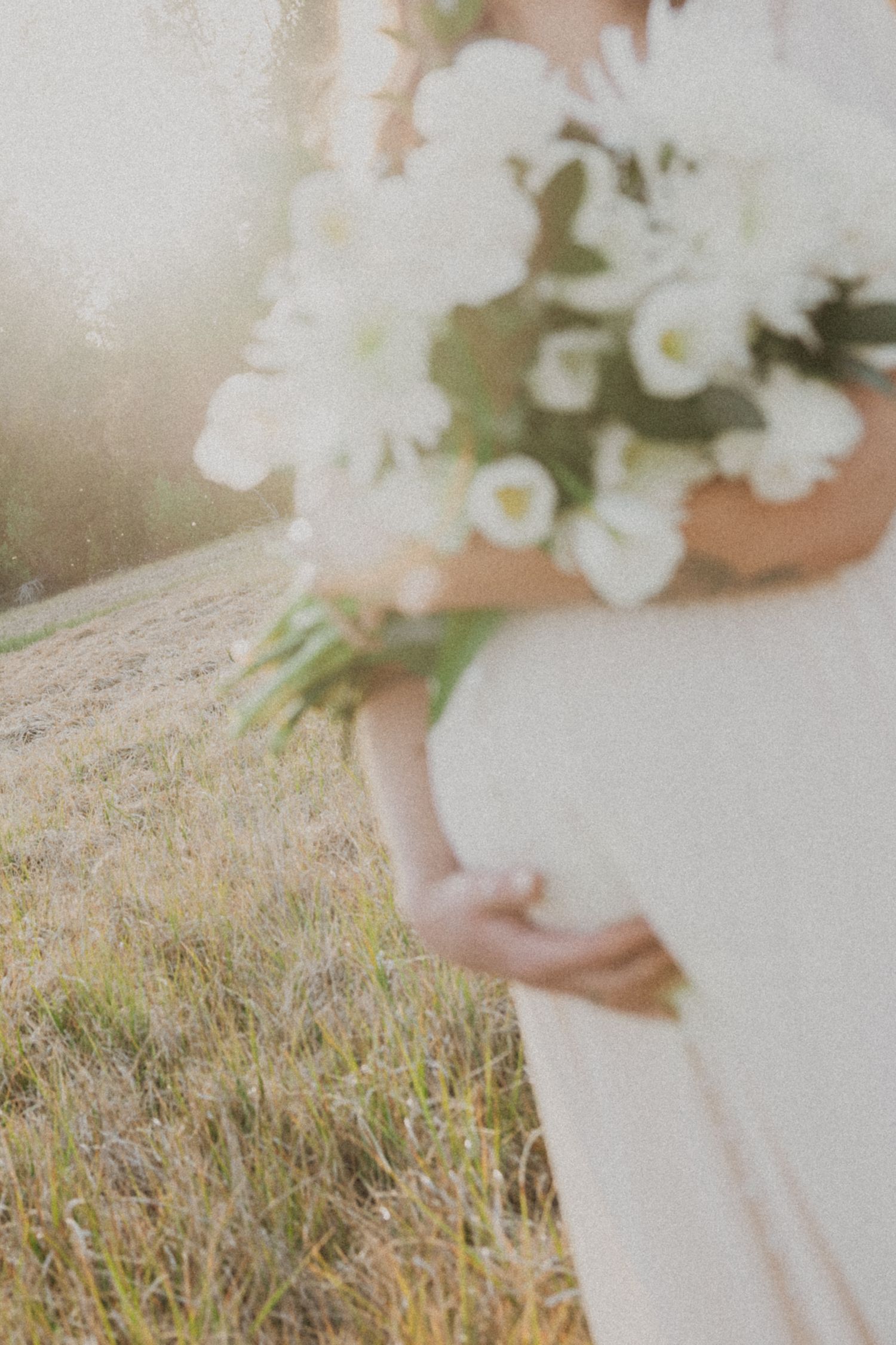 Bride in white dress holding a bouquet of white flowers in a sunlit field.