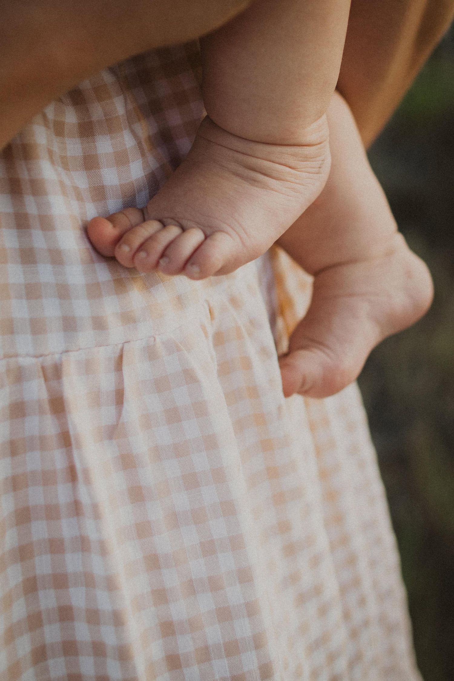 Close-up detail shot of bare feet against gingham fabric in soft natural lighting.