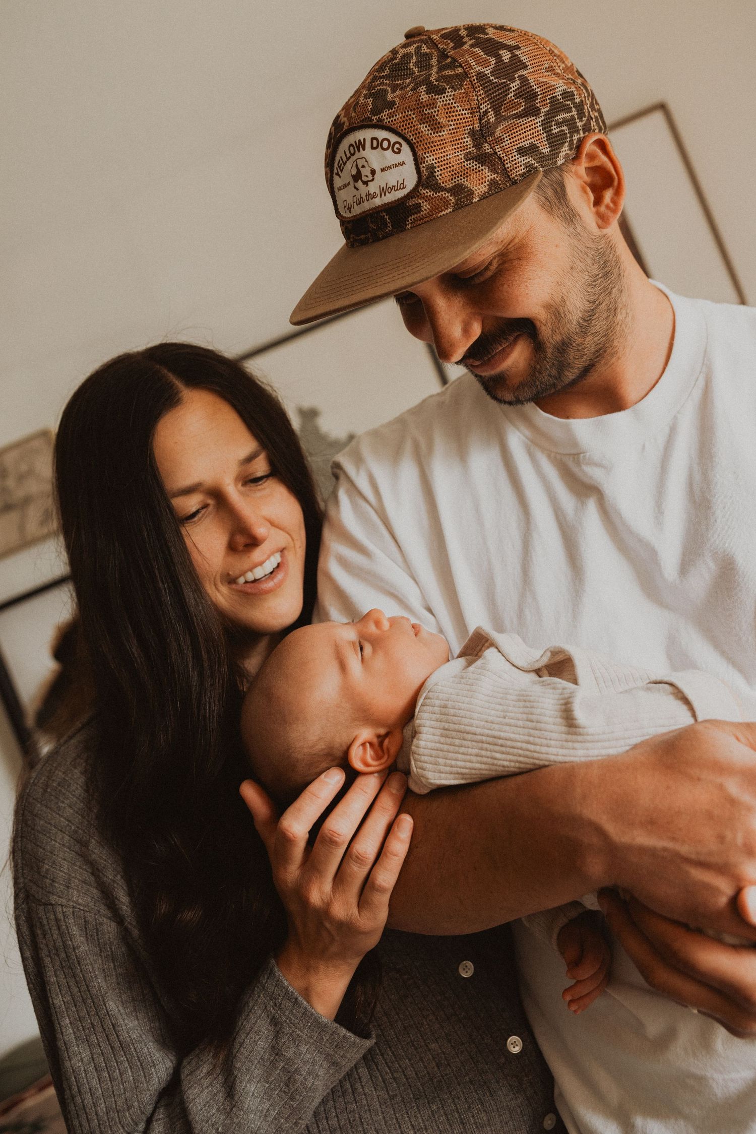 Smiling parents lovingly hold their sleeping newborn baby together in a warm, intimate family portrait.